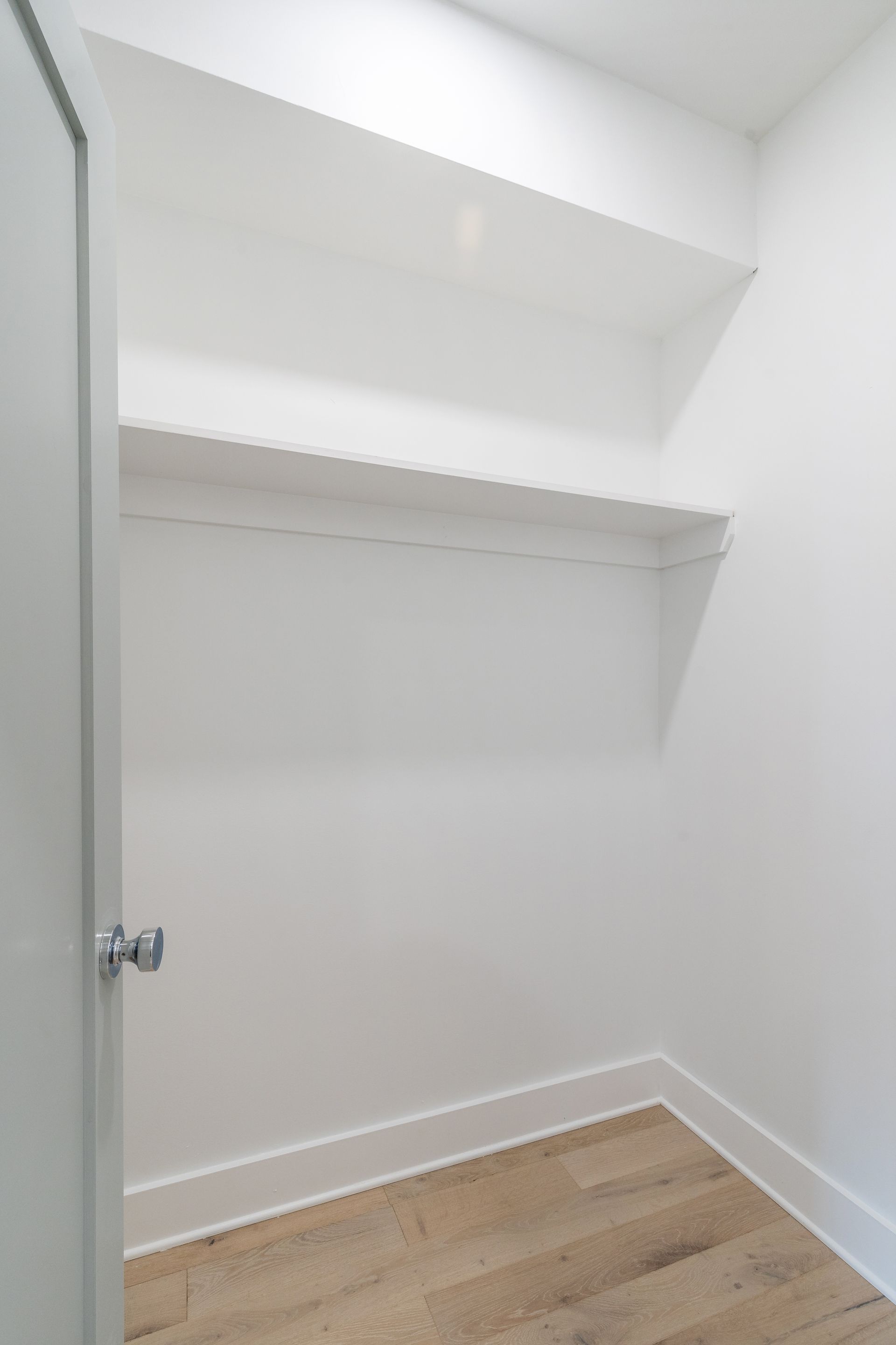 An empty walk in closet with white walls and wooden floors.