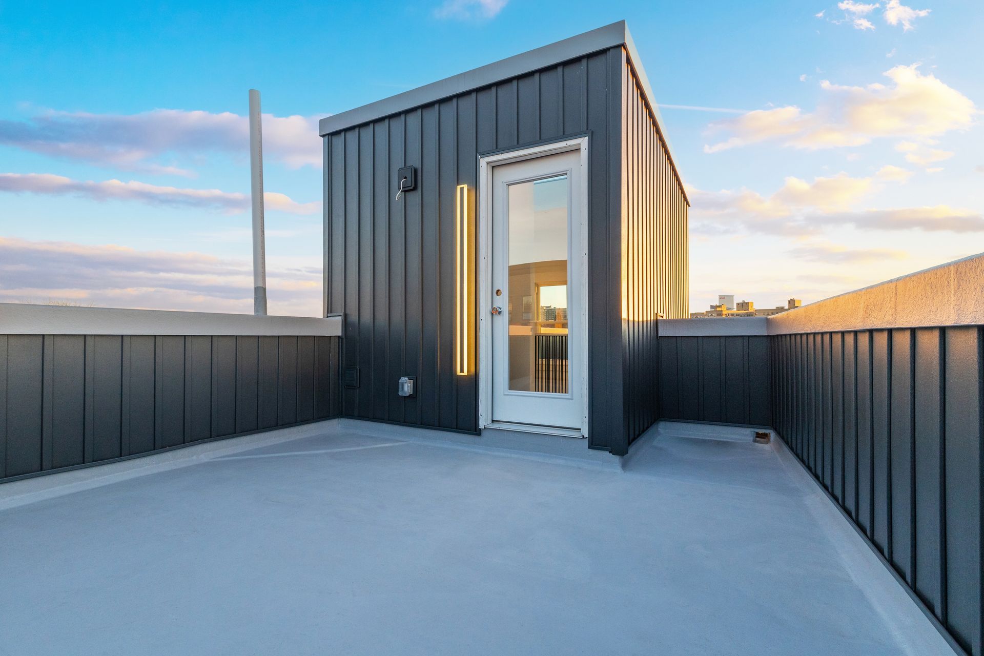 A rooftop deck with a black building and a white door.
