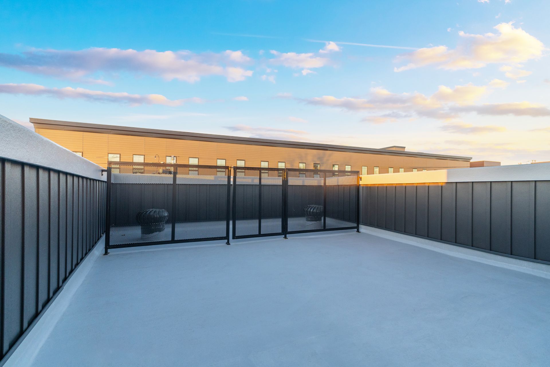 An empty rooftop deck with a fence and a building in the background.