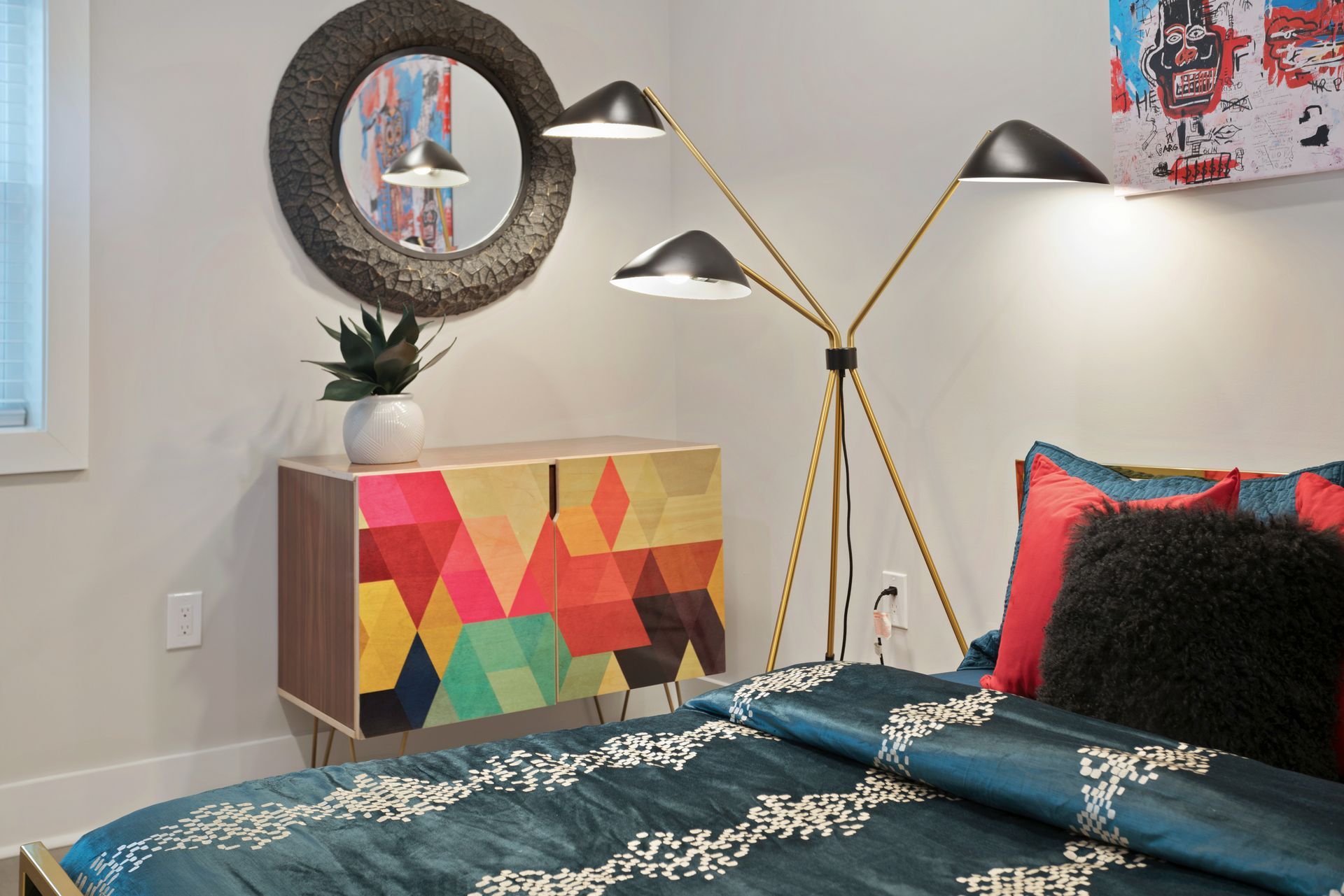 A bedroom with a bed , dresser , lamp and mirror.