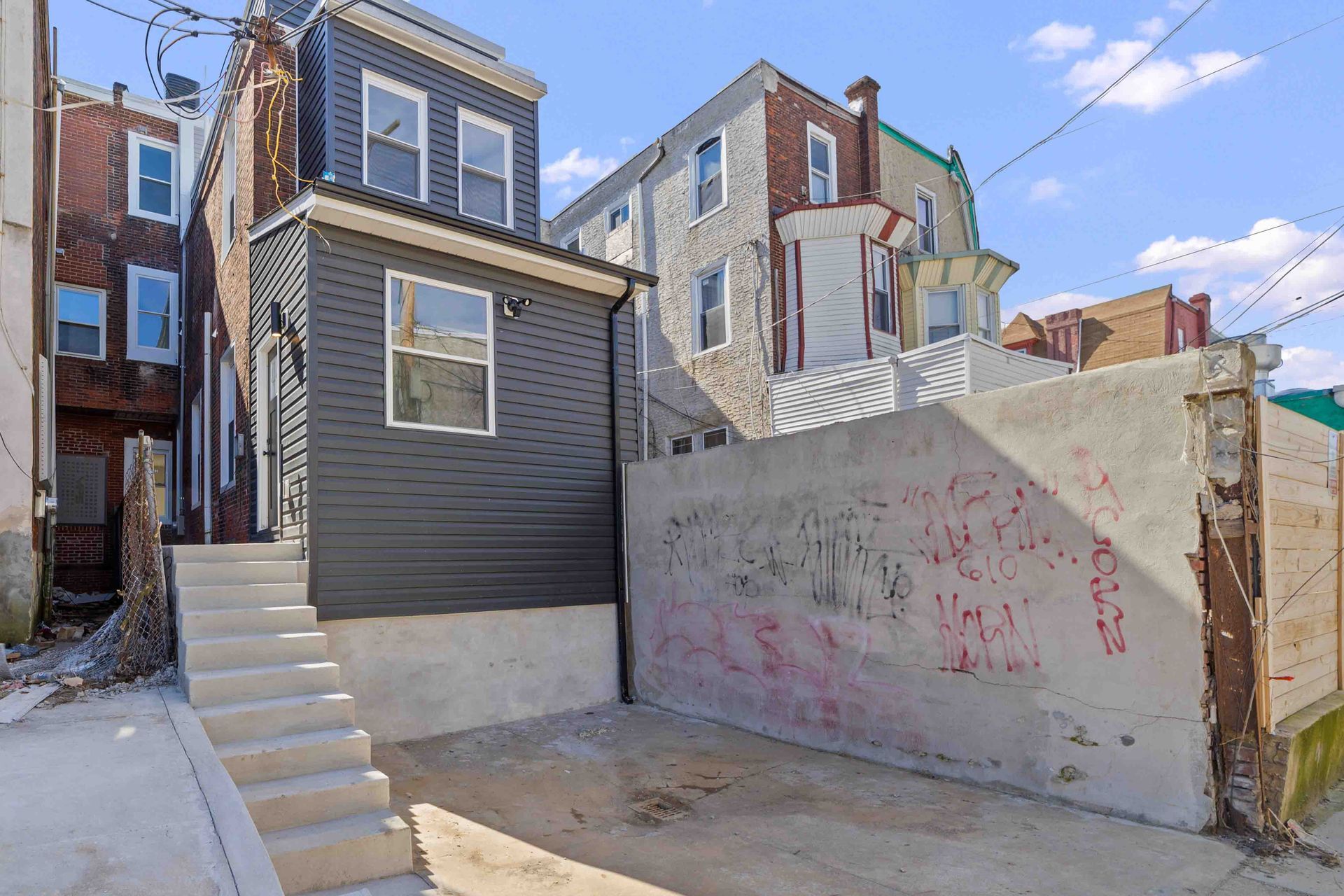 The backyard of a house with graffiti on the wall and stairs leading up to it.
