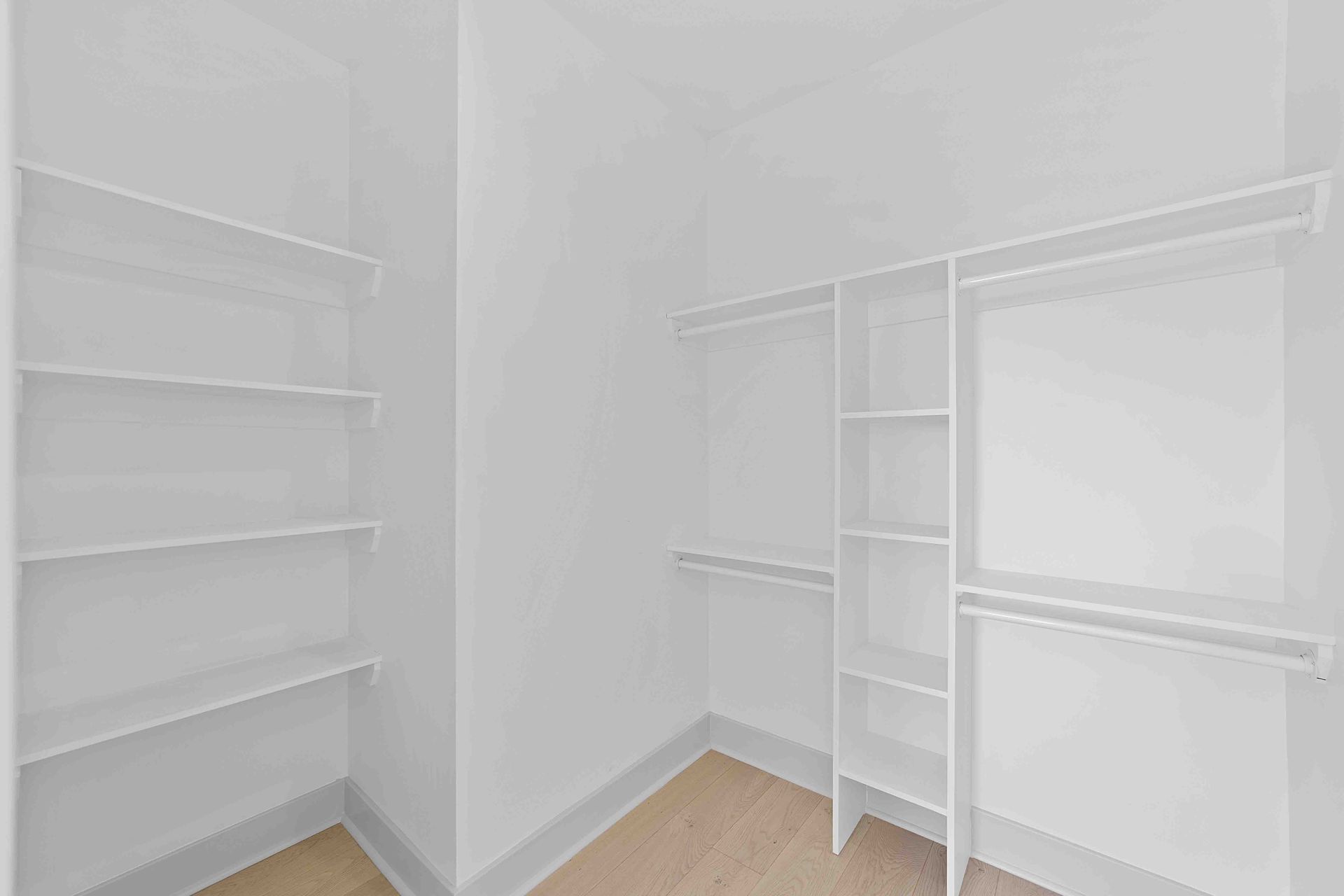 An empty walk in closet with white shelves and a wooden floor.