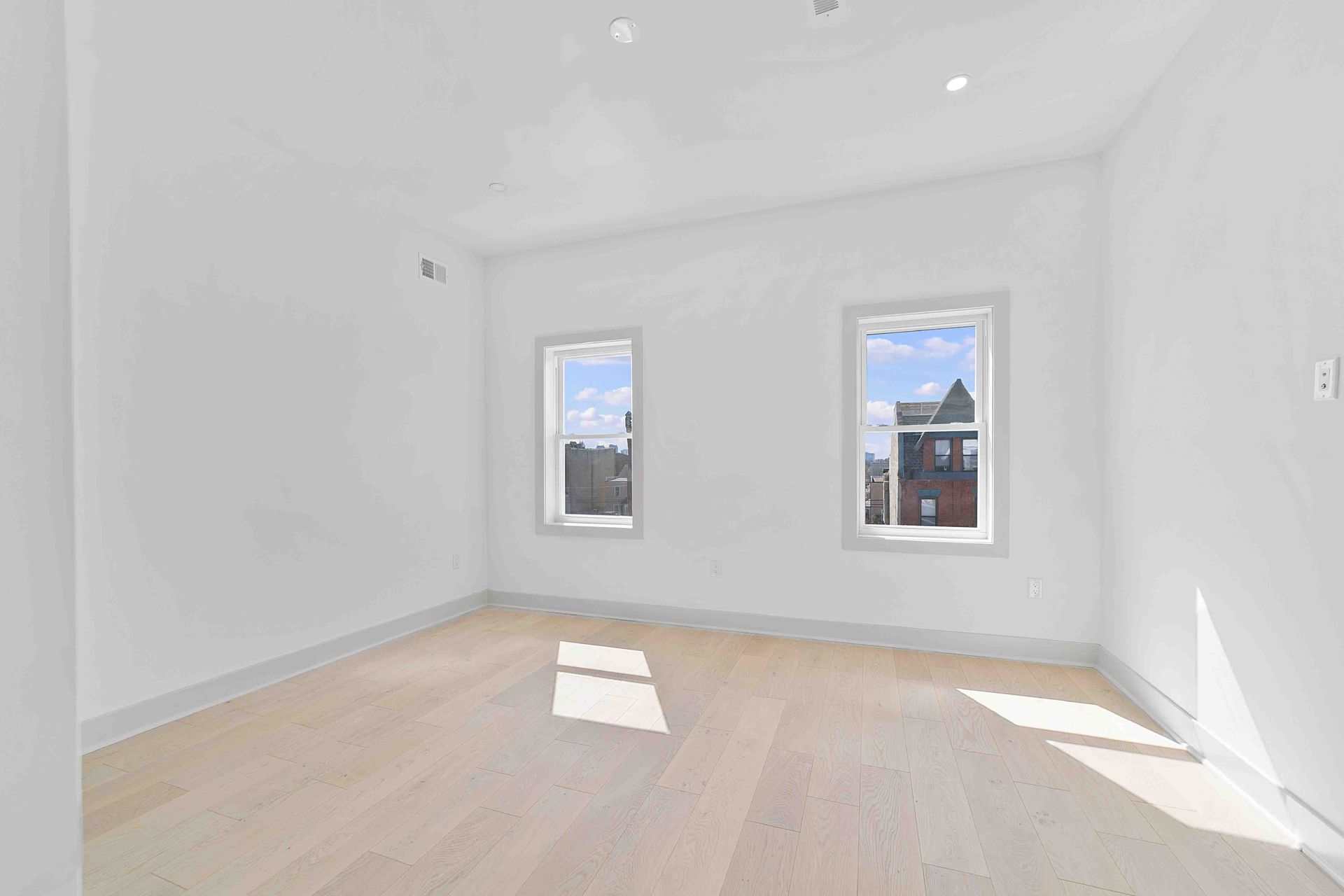 An empty room with hardwood floors and two windows.