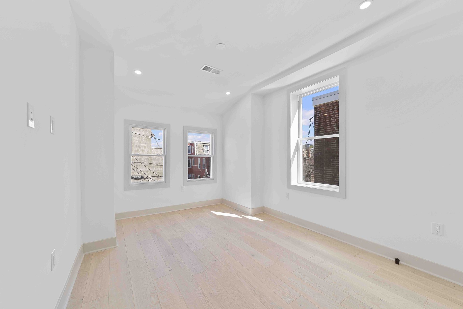 An empty room with hardwood floors and three windows.