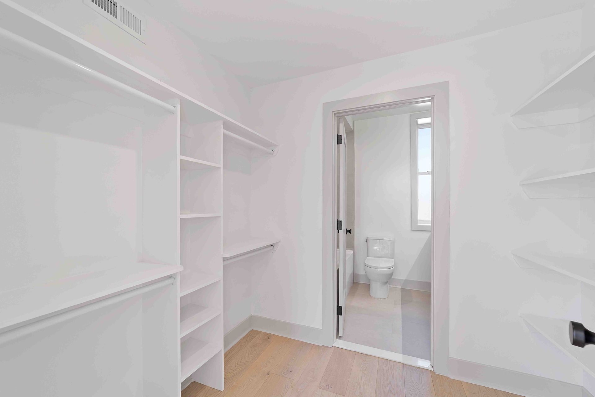 A walk in closet with white shelves and a toilet.