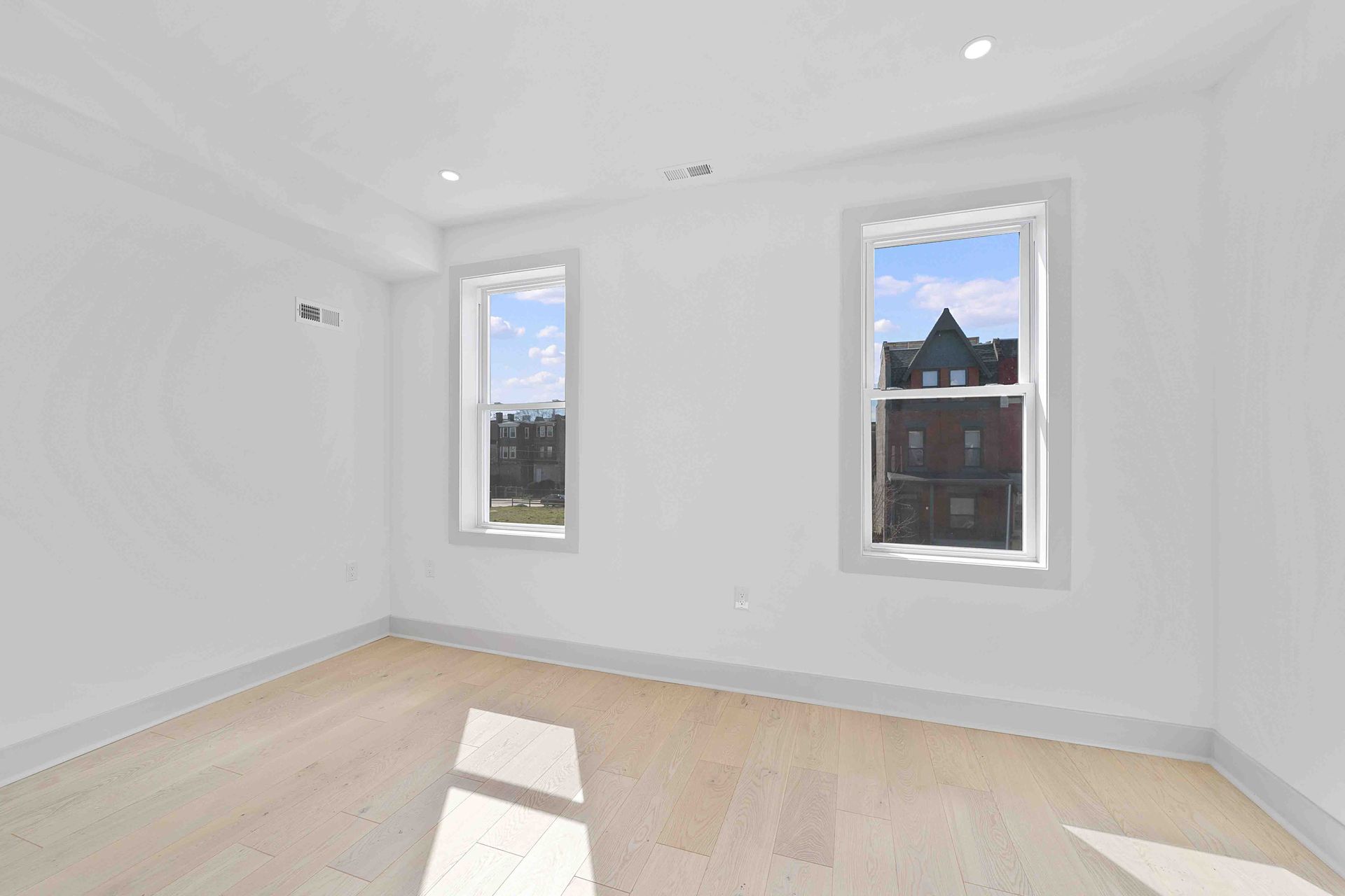 An empty room with two windows and hardwood floors.