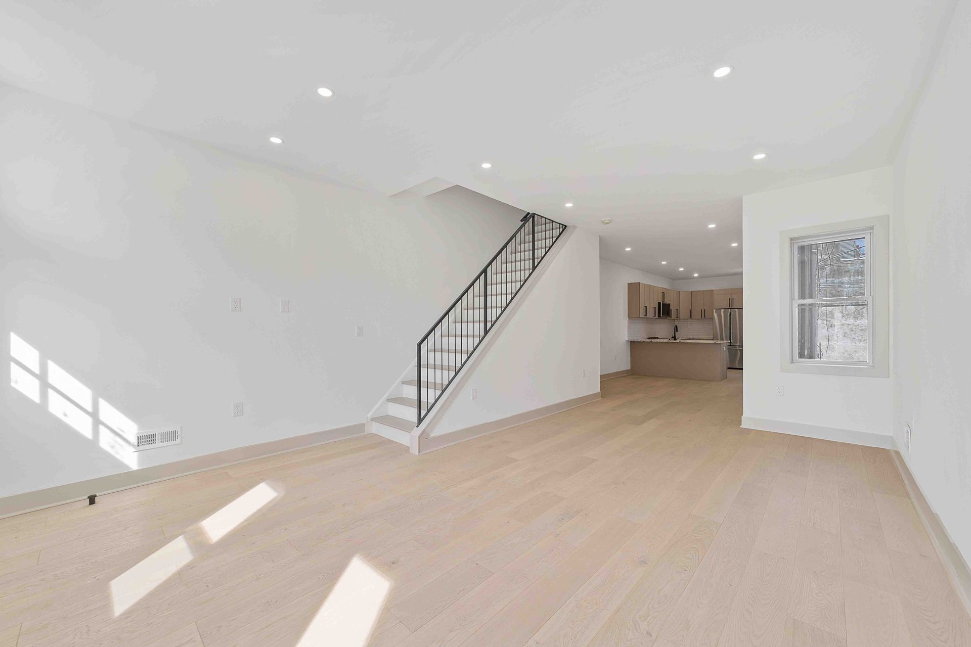 An empty living room with a staircase and a window.