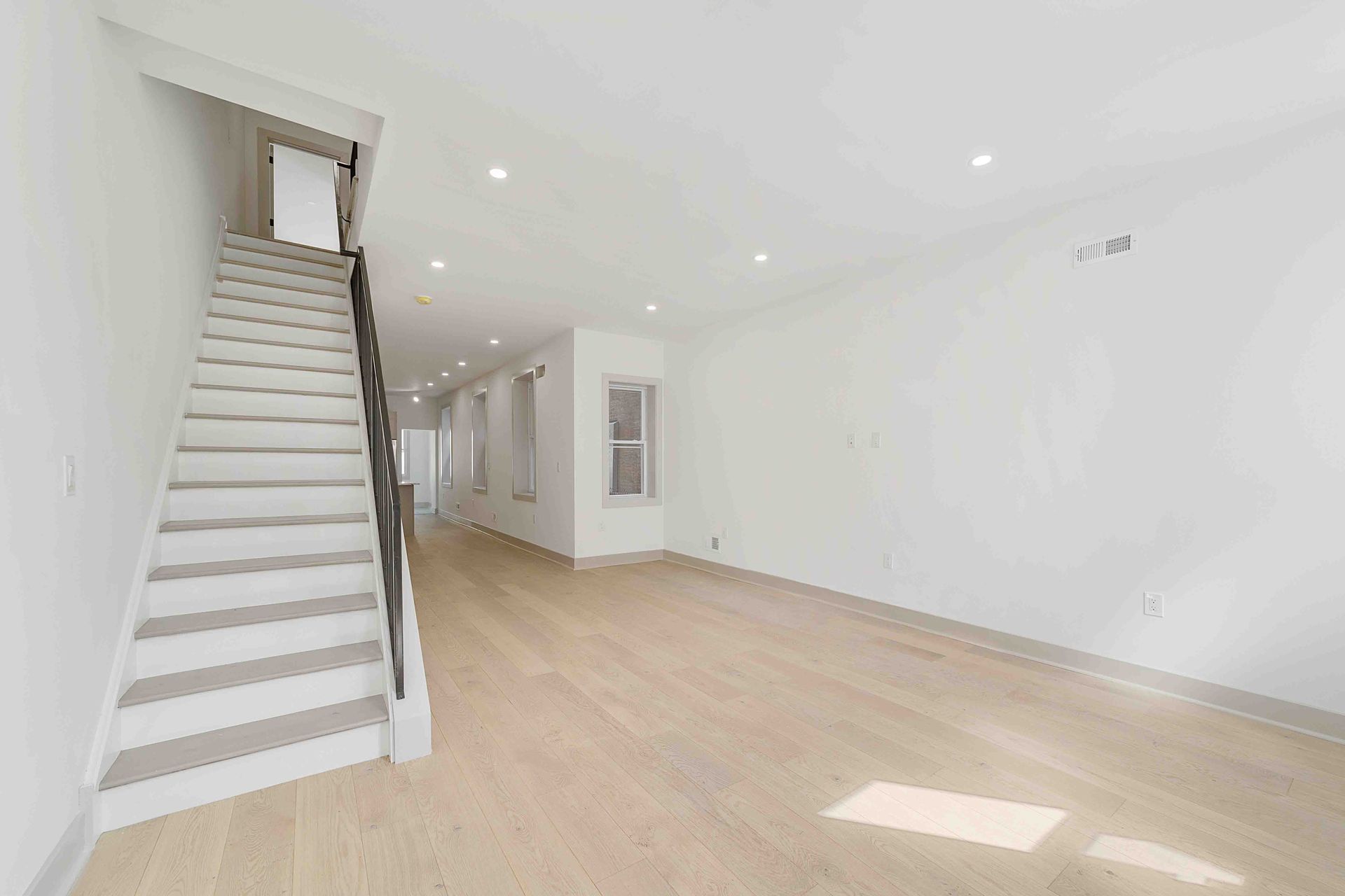 An empty living room with hardwood floors and stairs leading up to the second floor.