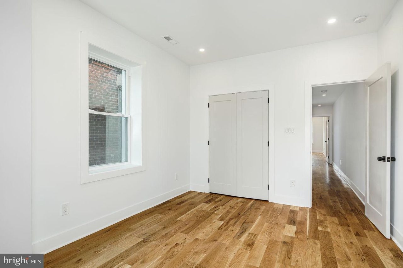 An empty bedroom with hardwood floors and white walls.