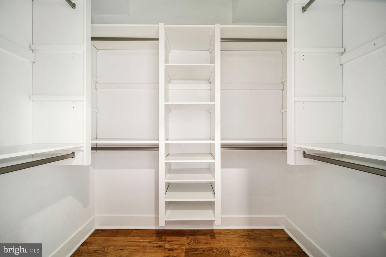 An empty walk in closet with white shelves and a ladder.