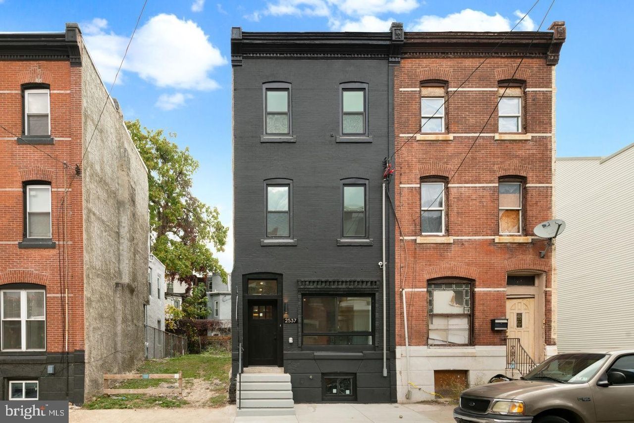 A black building is next to a brick building with a car parked in front of it.