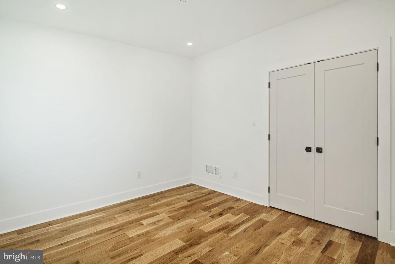An empty bedroom with hardwood floors and white walls.
