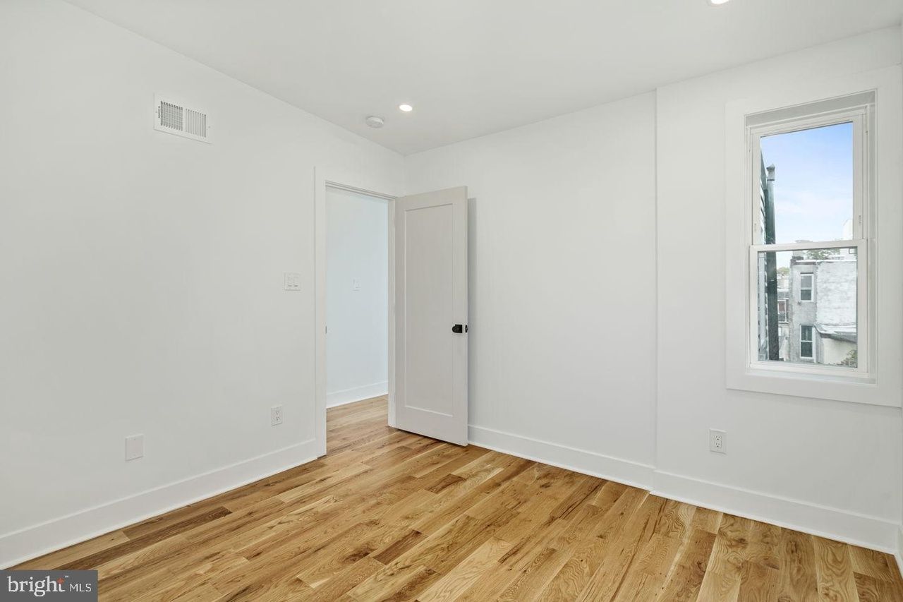 An empty bedroom with hardwood floors and white walls.