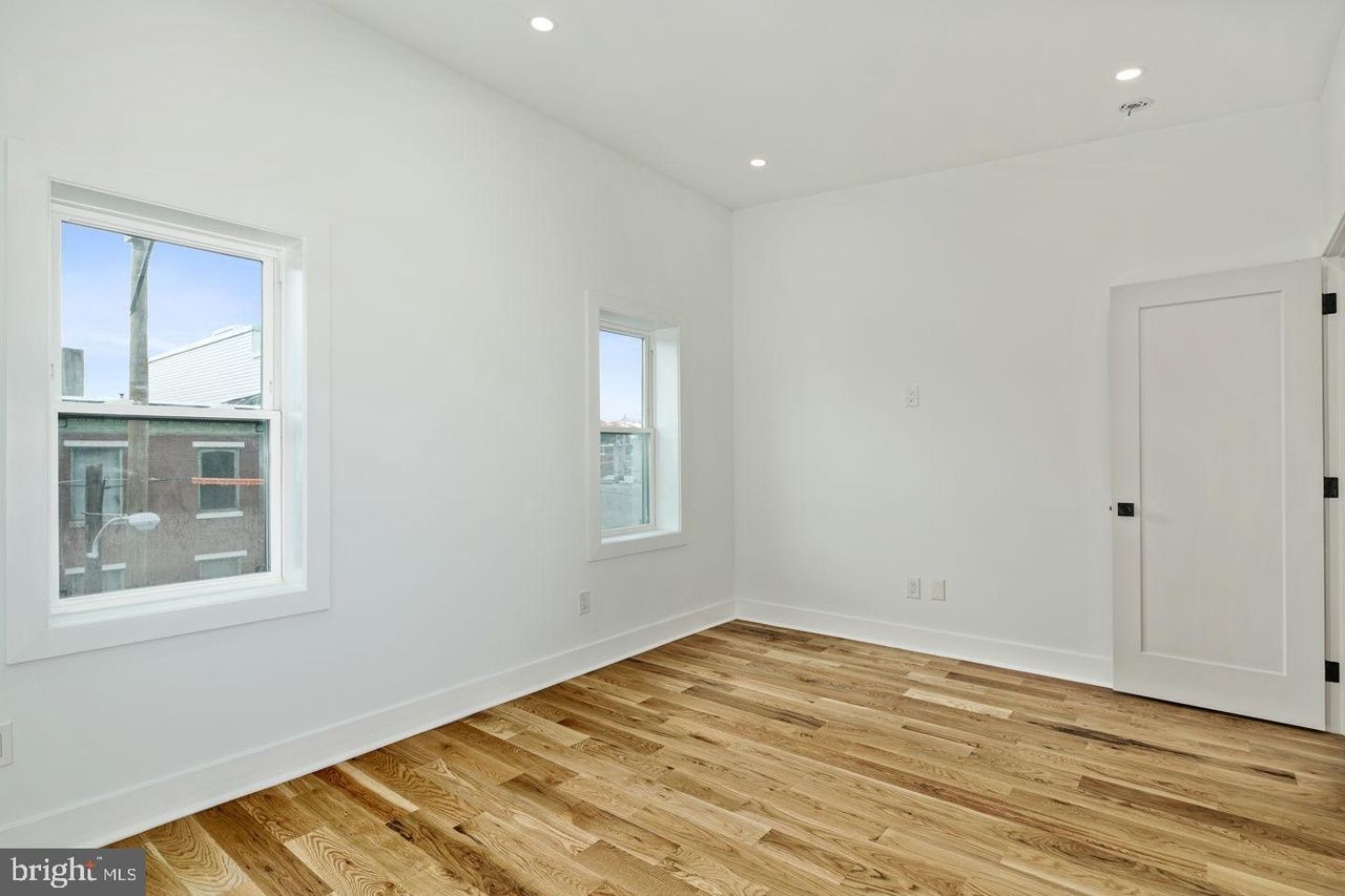 An empty bedroom with hardwood floors and two windows.