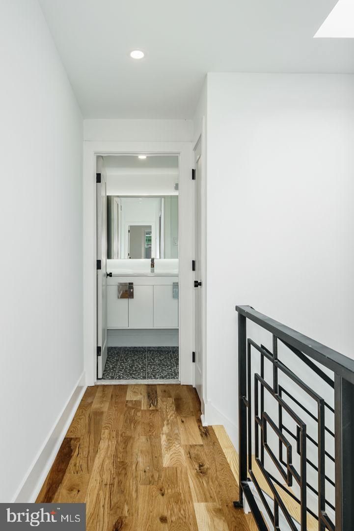 A hallway with hardwood floors and a bathroom in the background