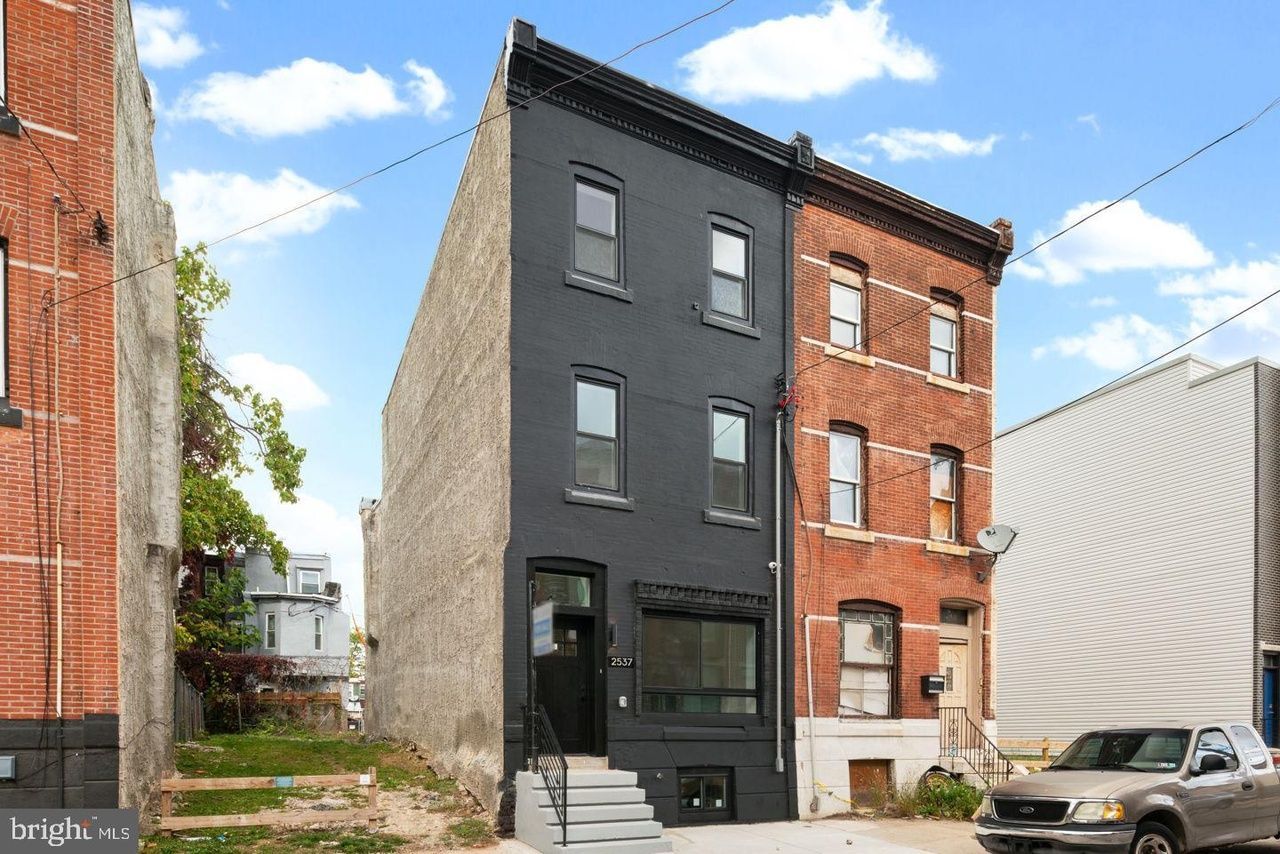 A black building is next to a brick building and a car is parked in front of it.