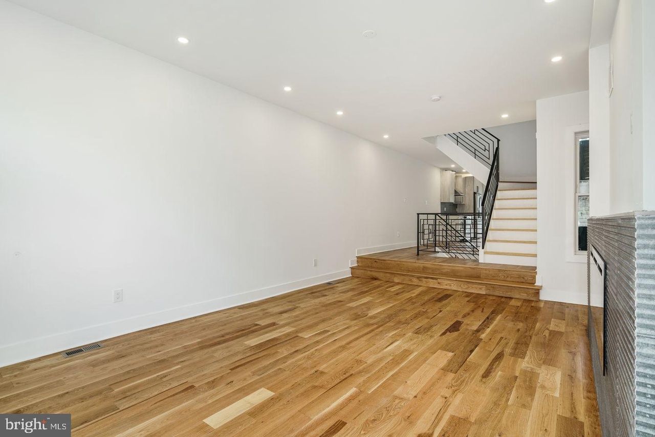 An empty living room with hardwood floors and white walls.