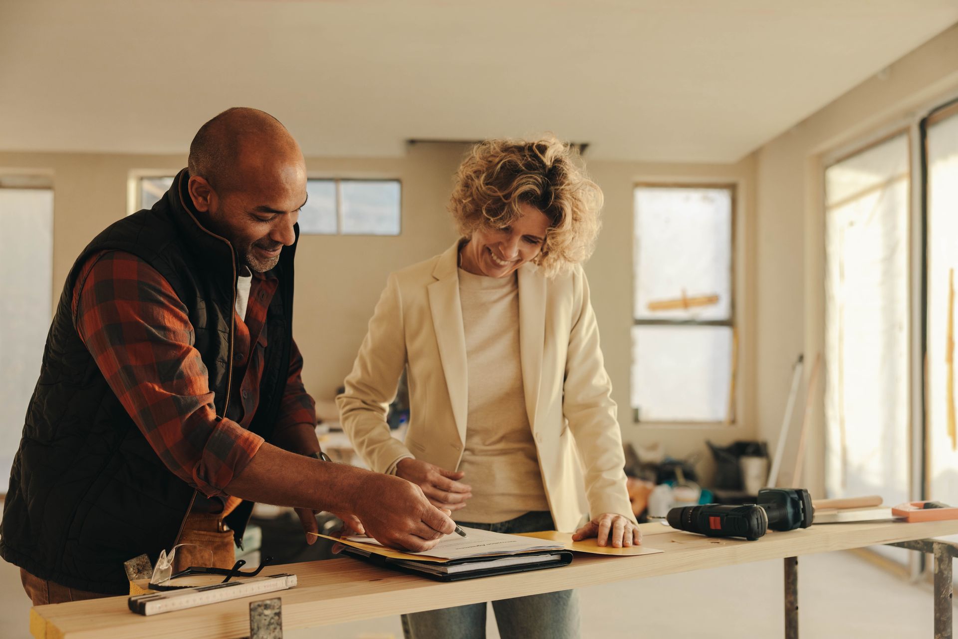 A man and a woman are standing at a table looking at a piece of paper.