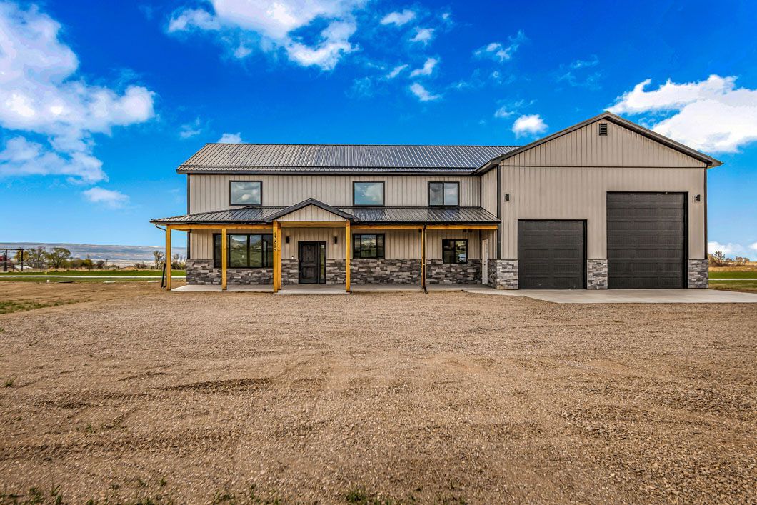 A large house with a garage and a porch is sitting on top of a dirt field.
