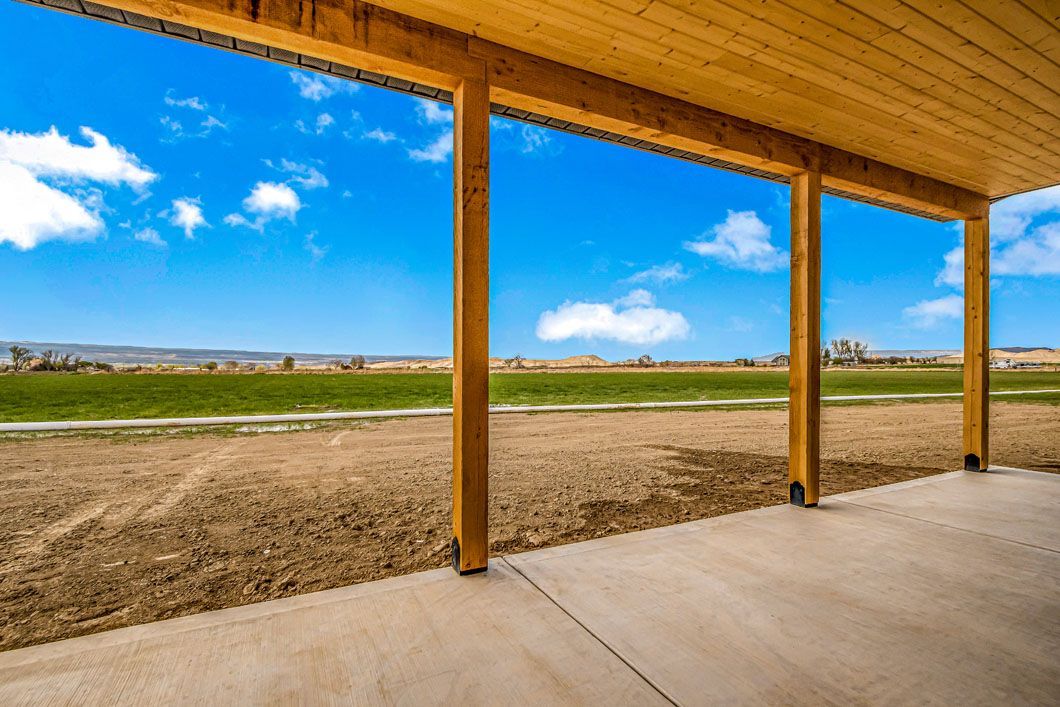 A covered porch with a view of a field and a blue sky.