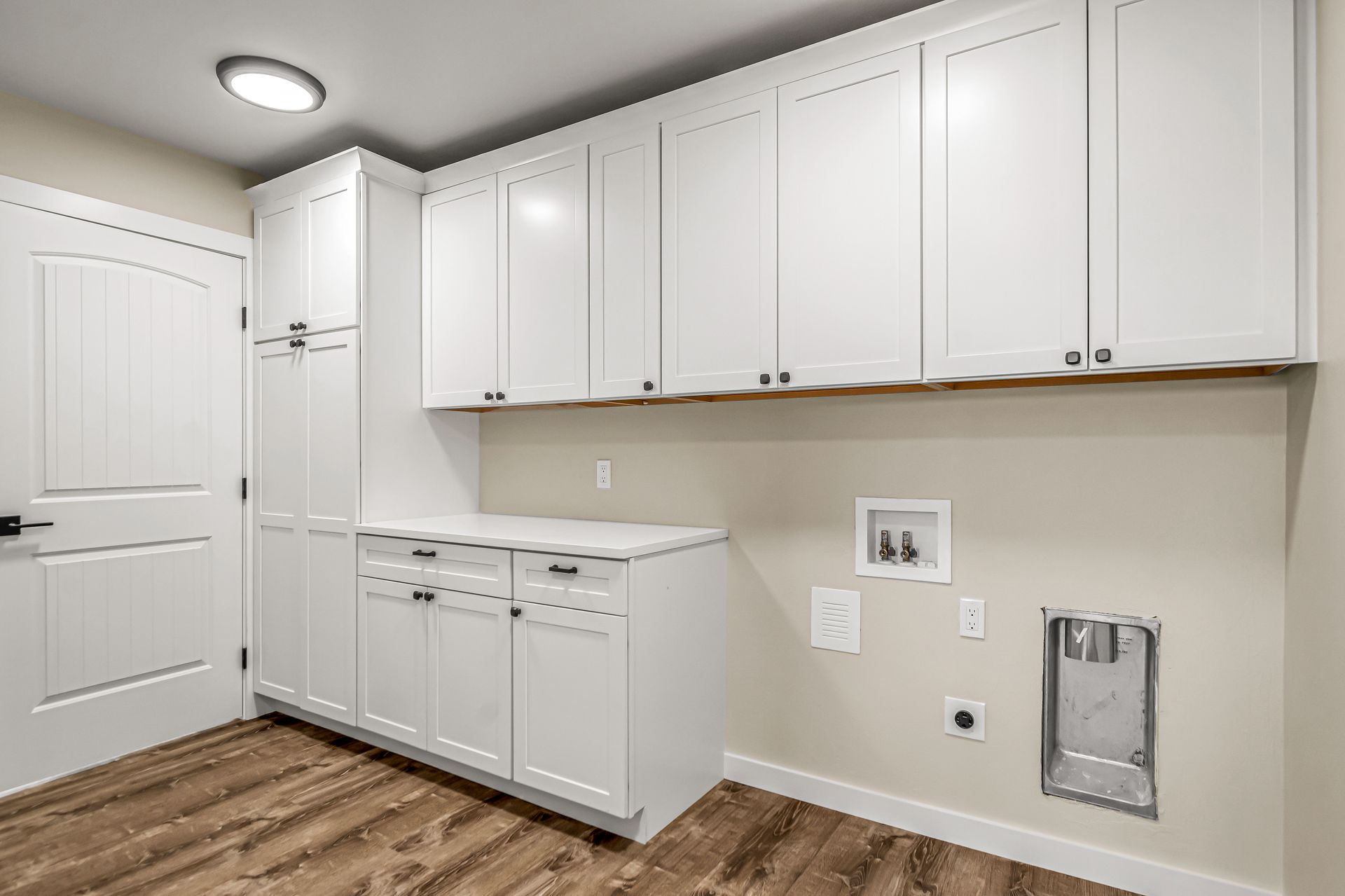 A laundry room with white cabinets and hardwood floors.