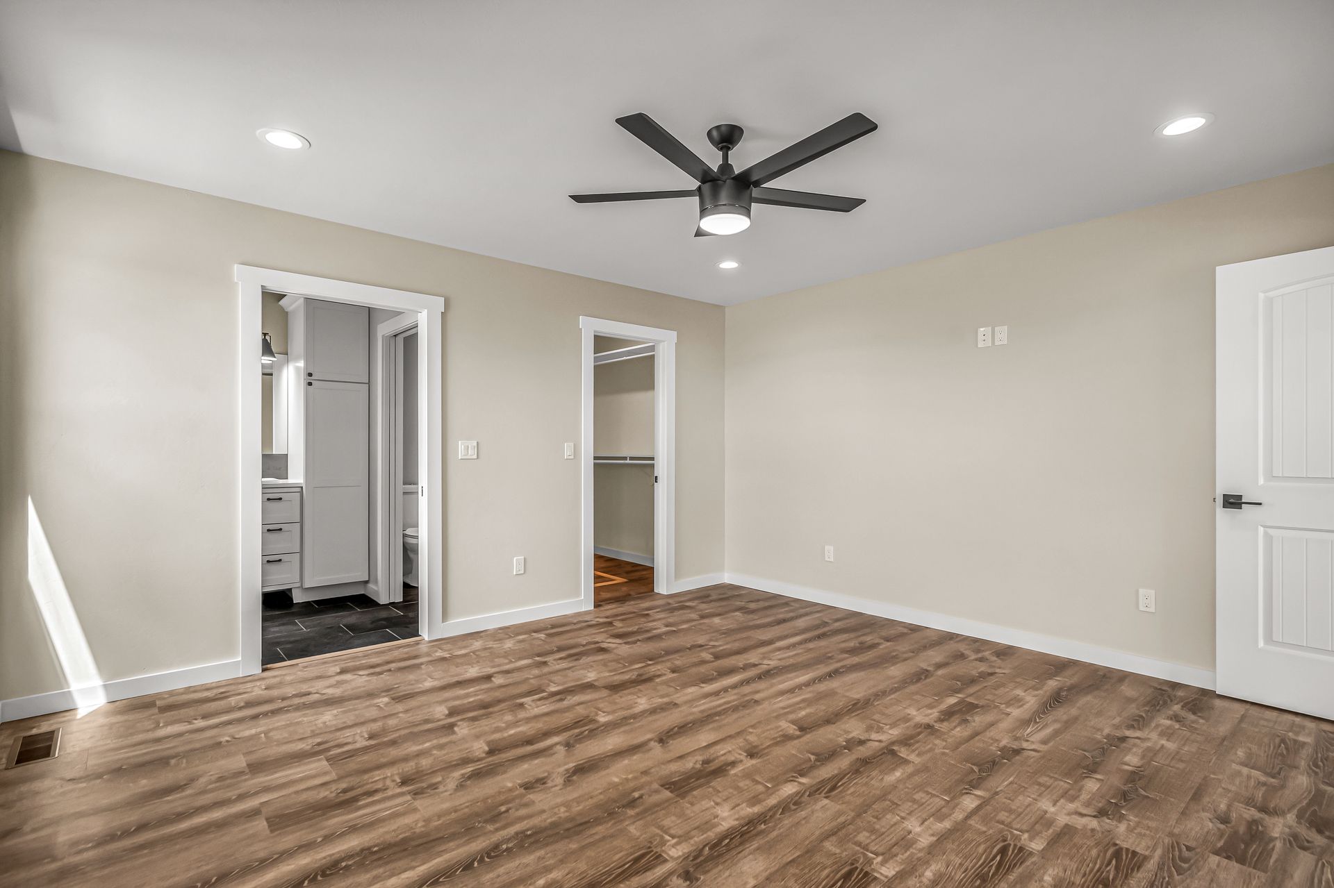 A large empty room with hardwood floors and a ceiling fan.