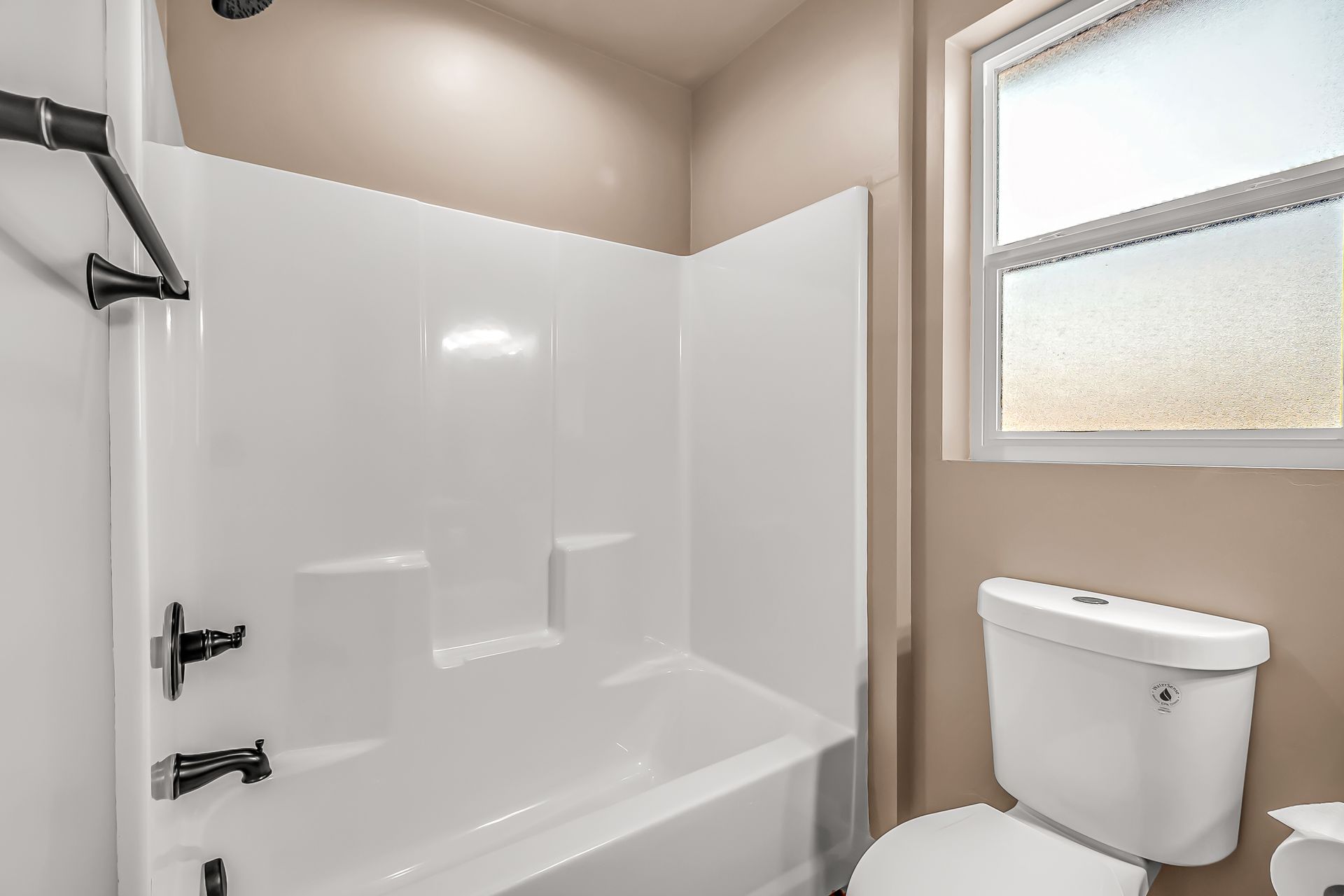 A bathroom with a toilet , bathtub , shower and window.