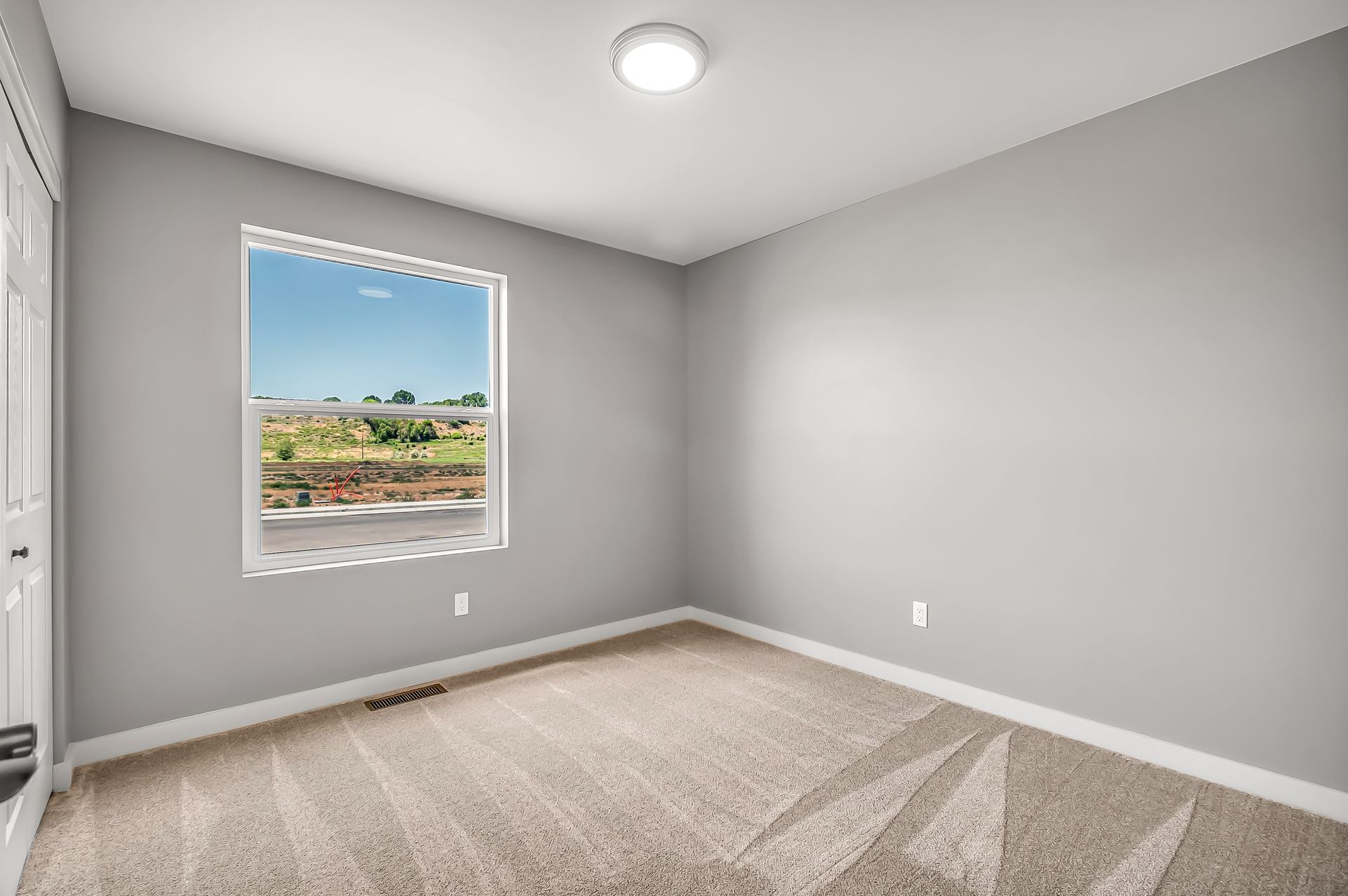 An empty bedroom with a window and a carpeted floor.