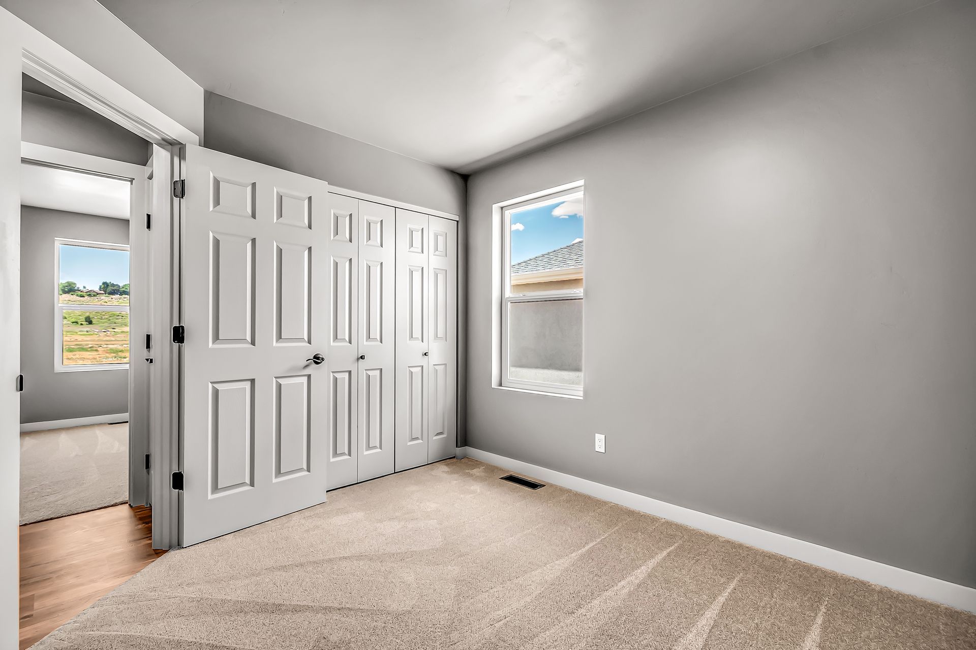 An empty bedroom with a large closet and two windows.