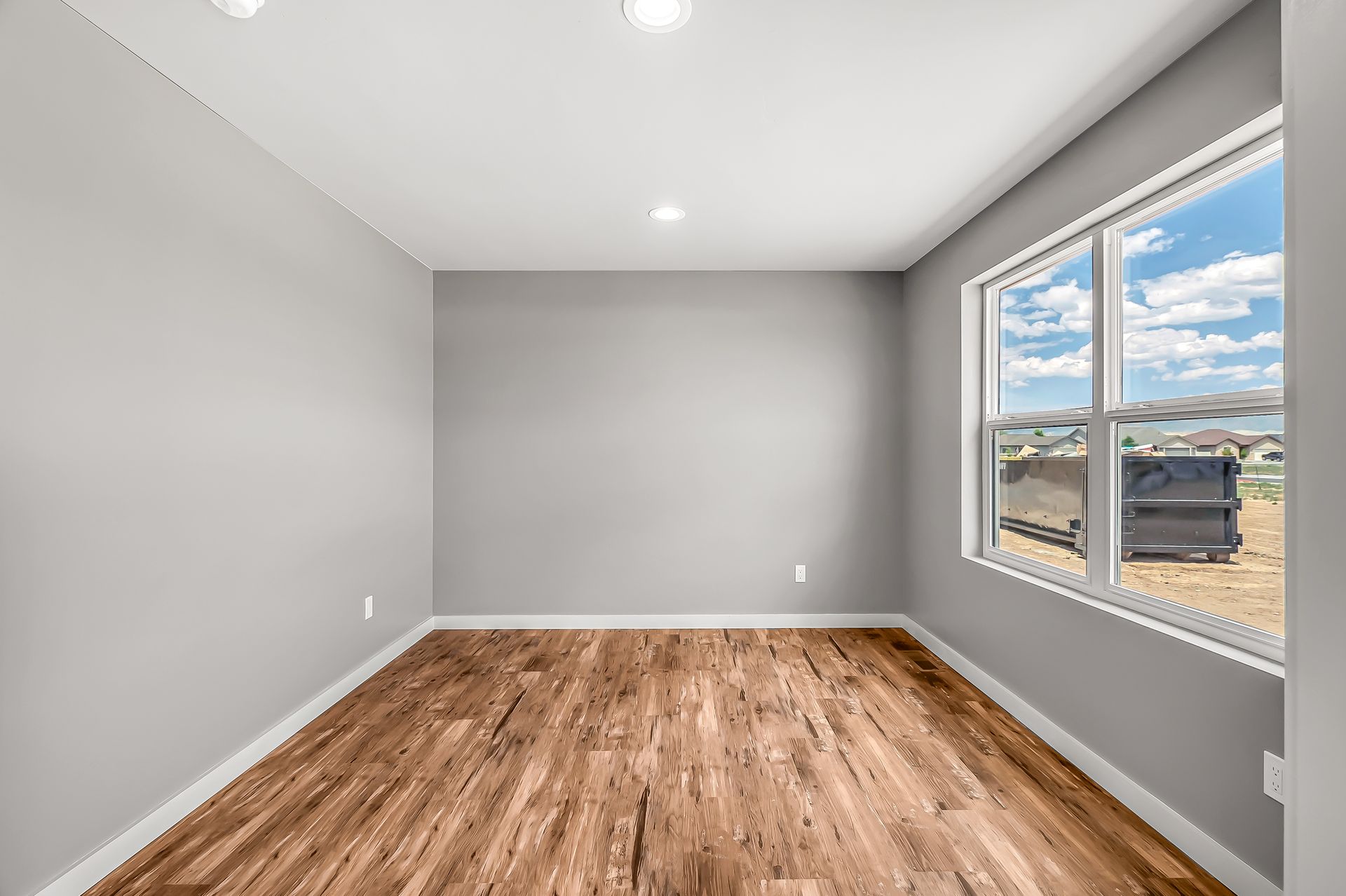 An empty room with hardwood floors and two windows.