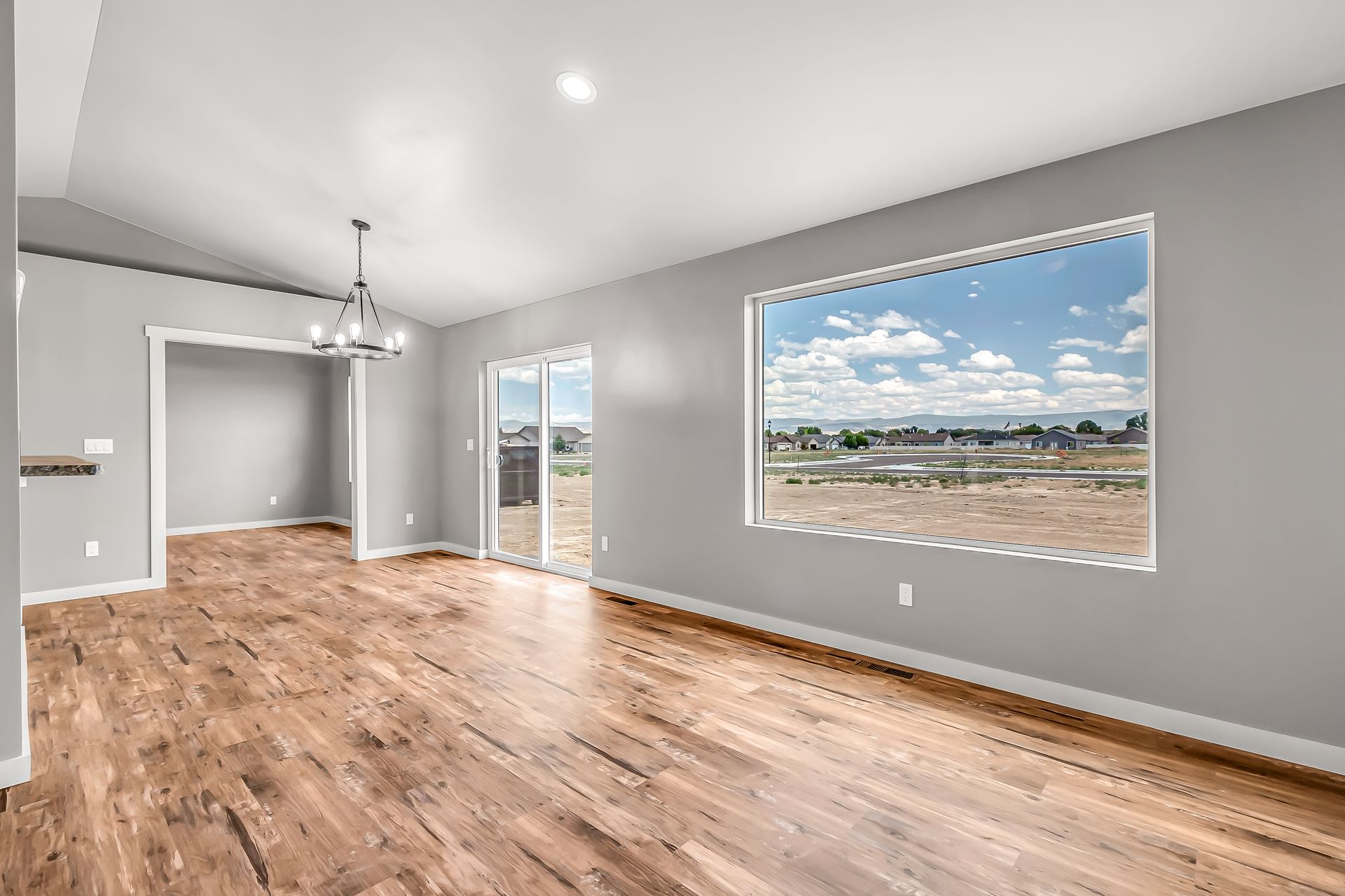 An empty living room with hardwood floors and a large window.