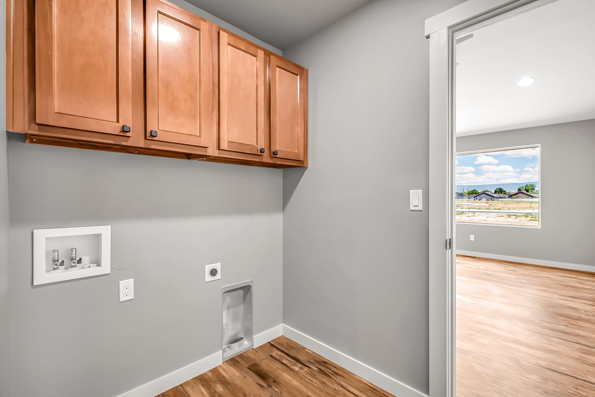 A laundry room in a house with wooden cabinets and a window.