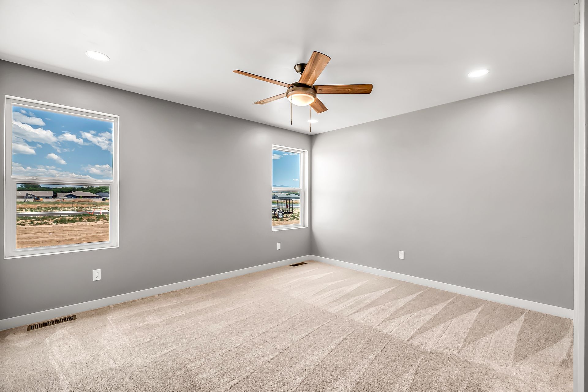 An empty bedroom with a ceiling fan and two windows.
