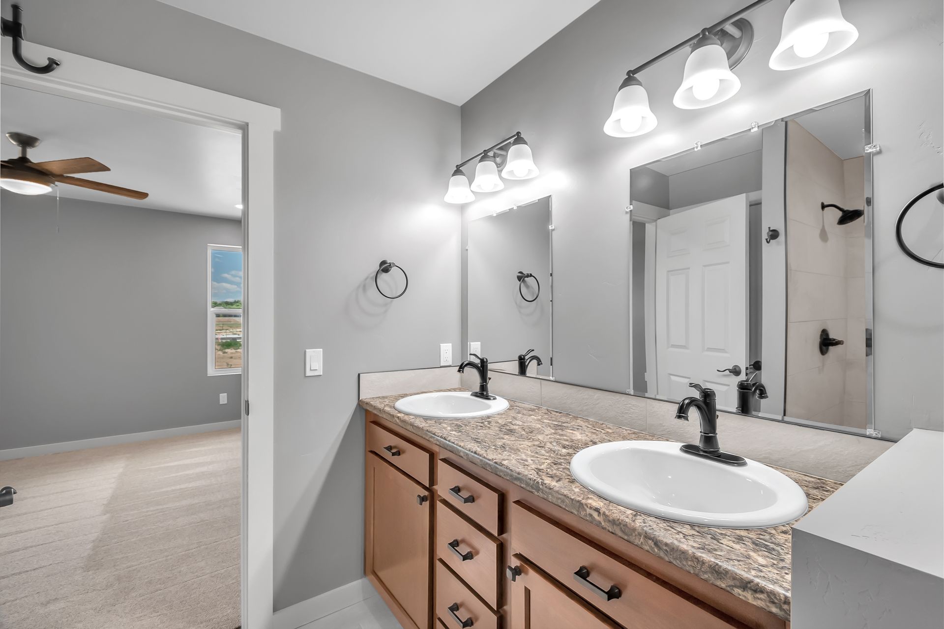 A bathroom with two sinks , two mirrors and a ceiling fan.