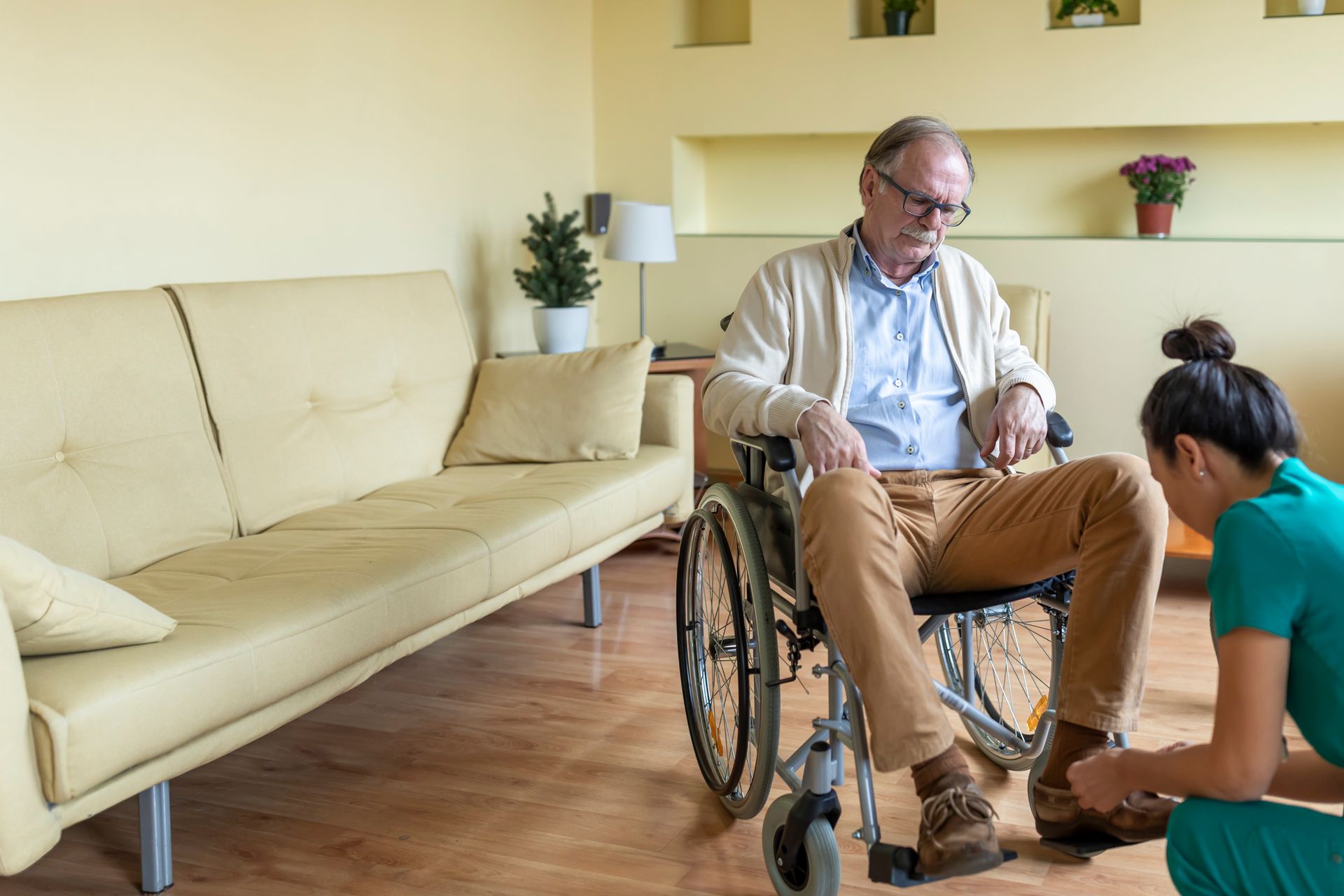 An elderly man in a wheelchair is being helped by a nurse.