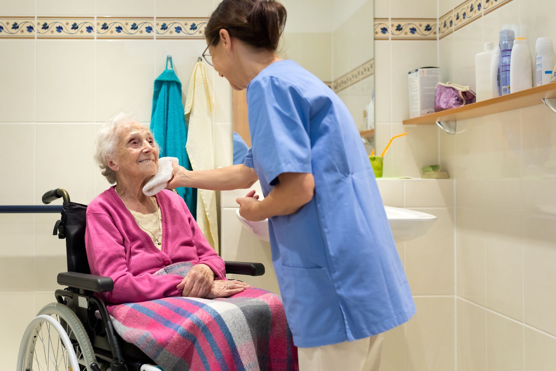 An elderly woman in a wheelchair is being helped by a nurse in a bathroom.
