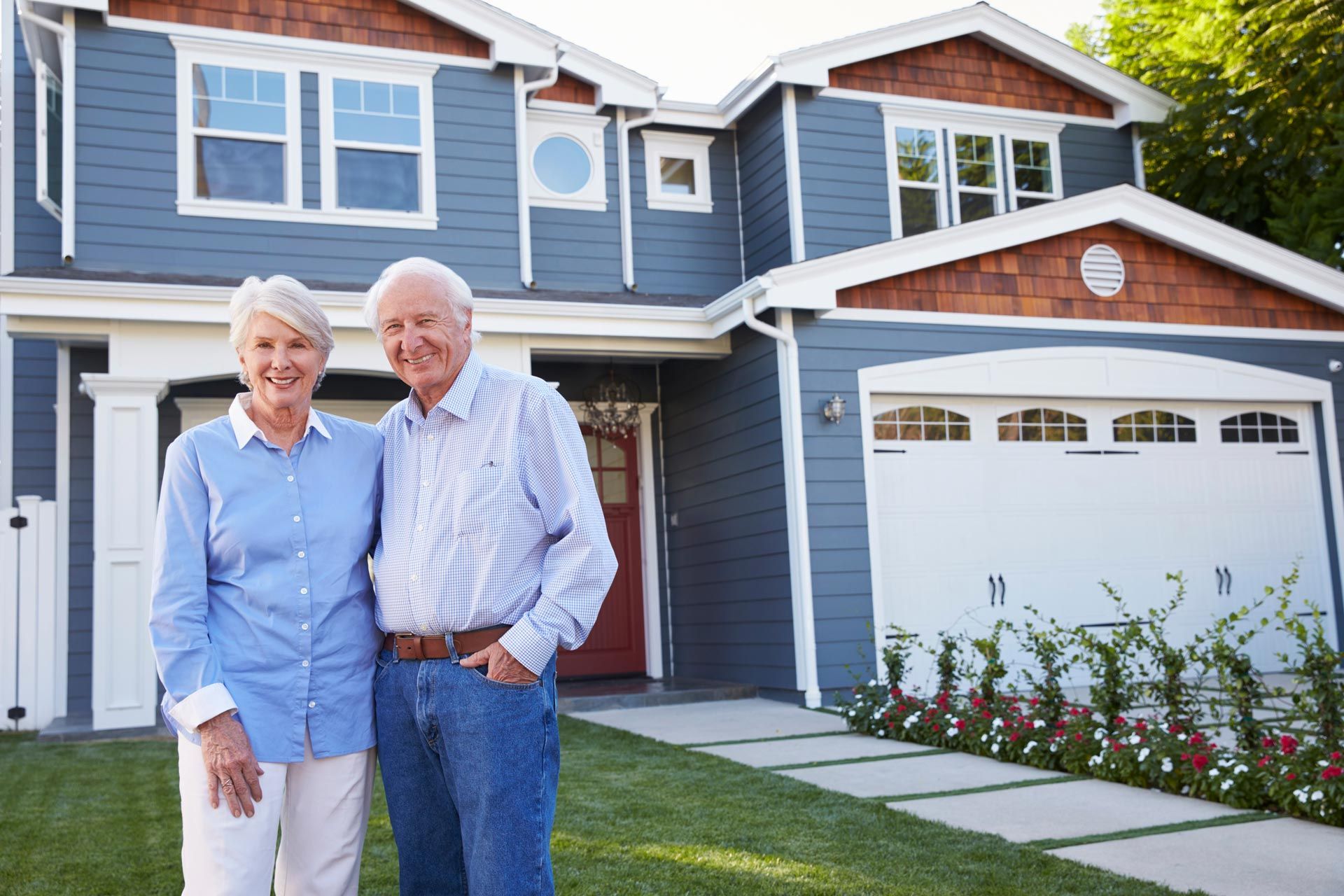 Couple smiles in front of a blue house with white trim and a two-car garage.
