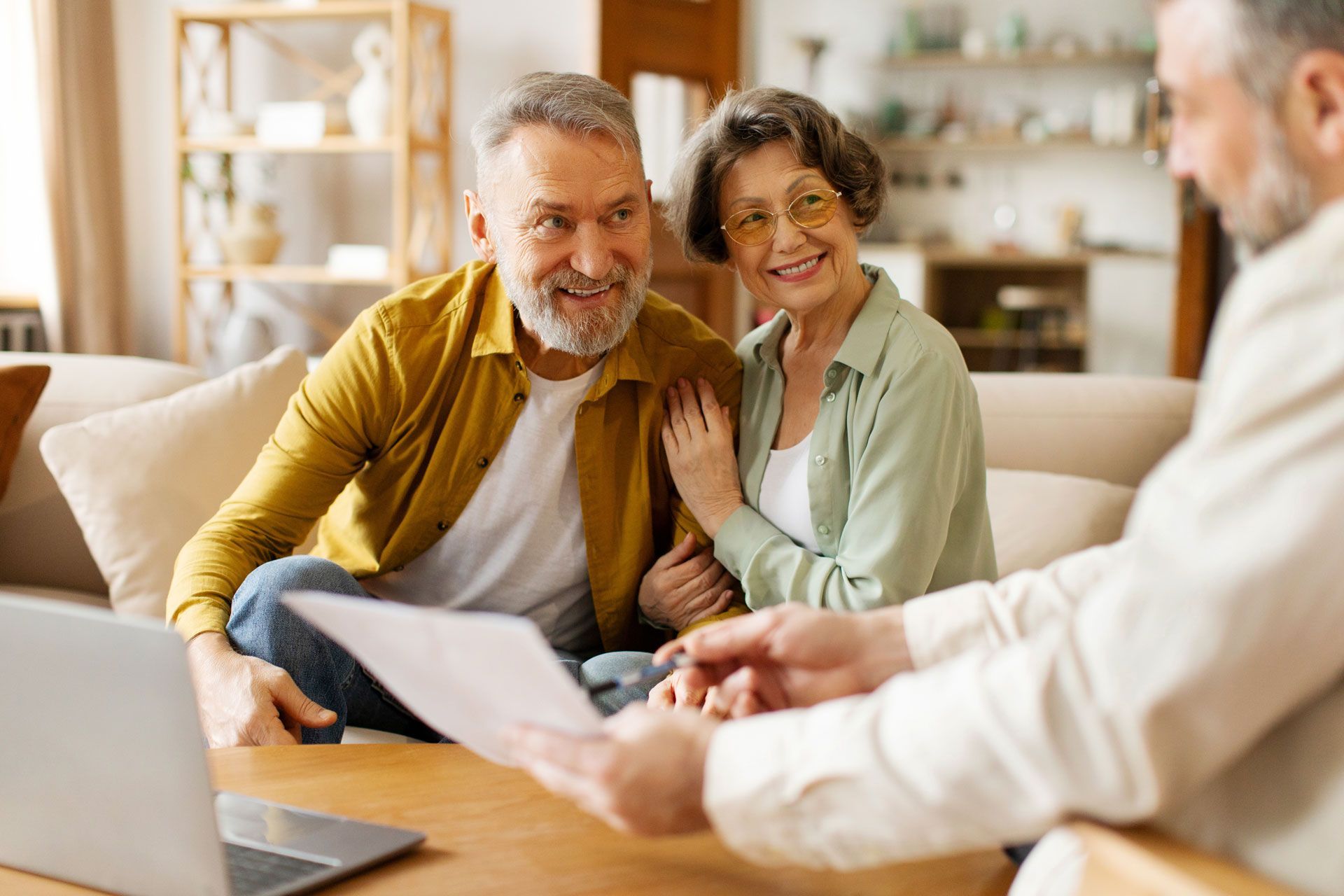 Older couple smiles while reviewing documents with a professional, in a home setting.