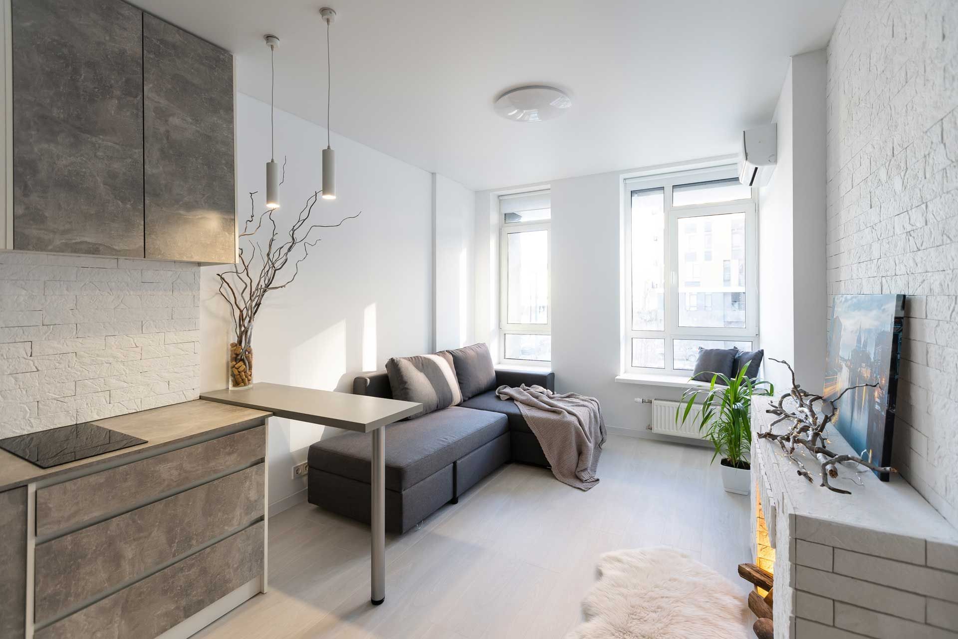 Small, modern apartment with gray kitchen and sofa, white walls, and fireplace.