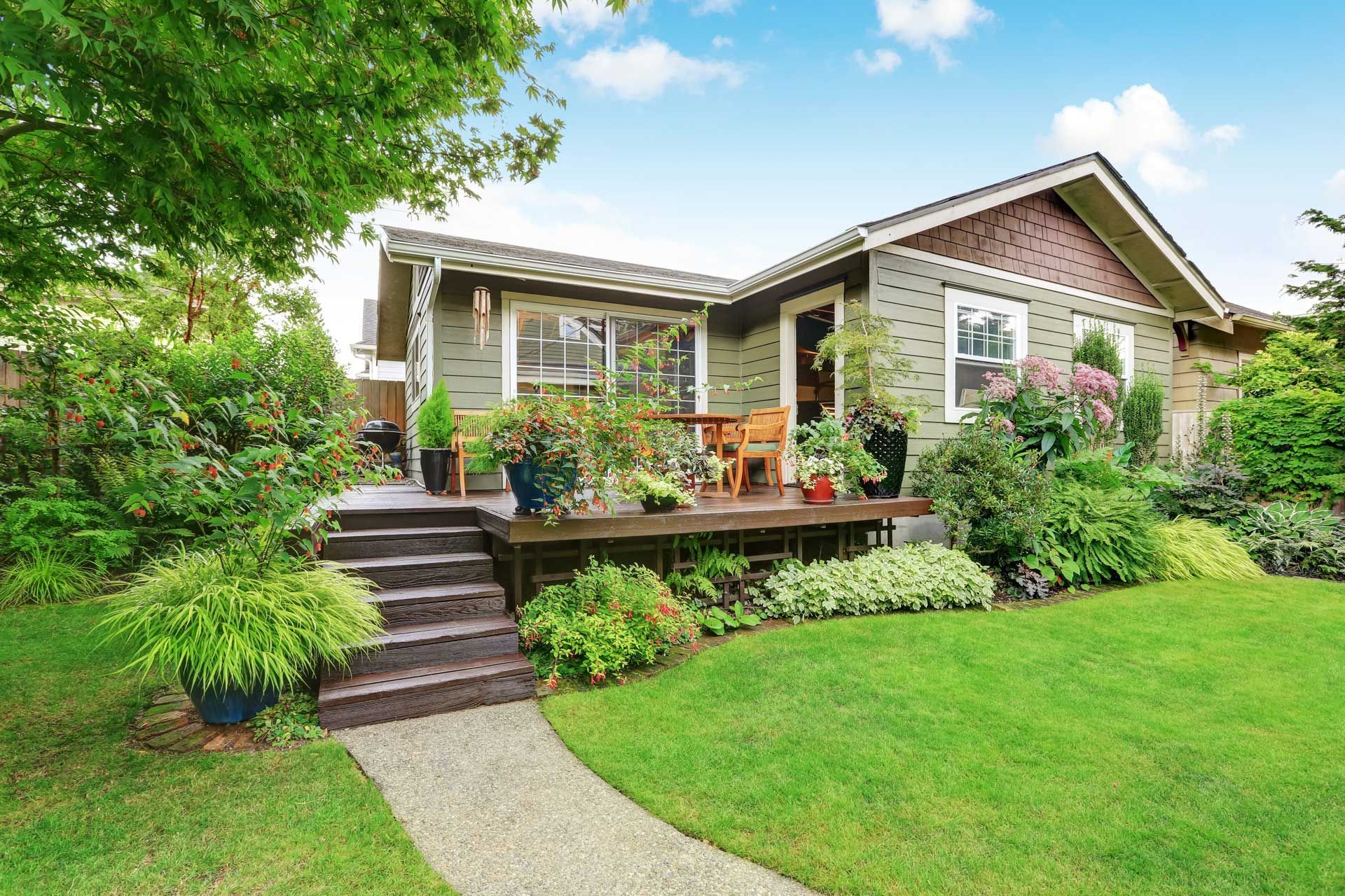 Green house with a front porch and lush landscaping, pathway leading through the green lawn.