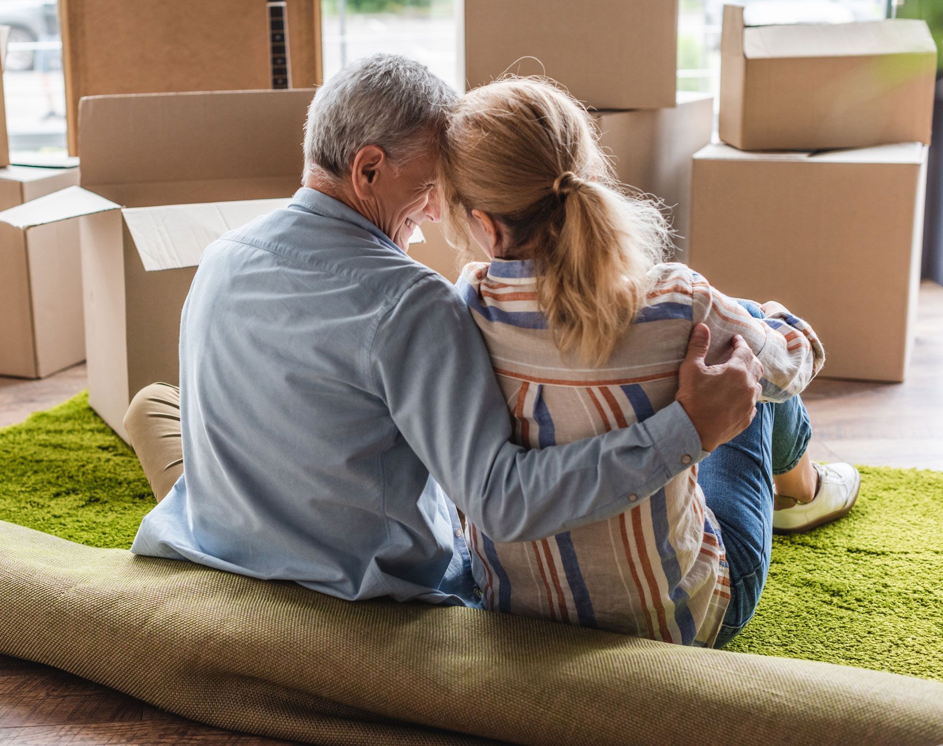 Couple embraces on a green rug in a room with moving boxes.