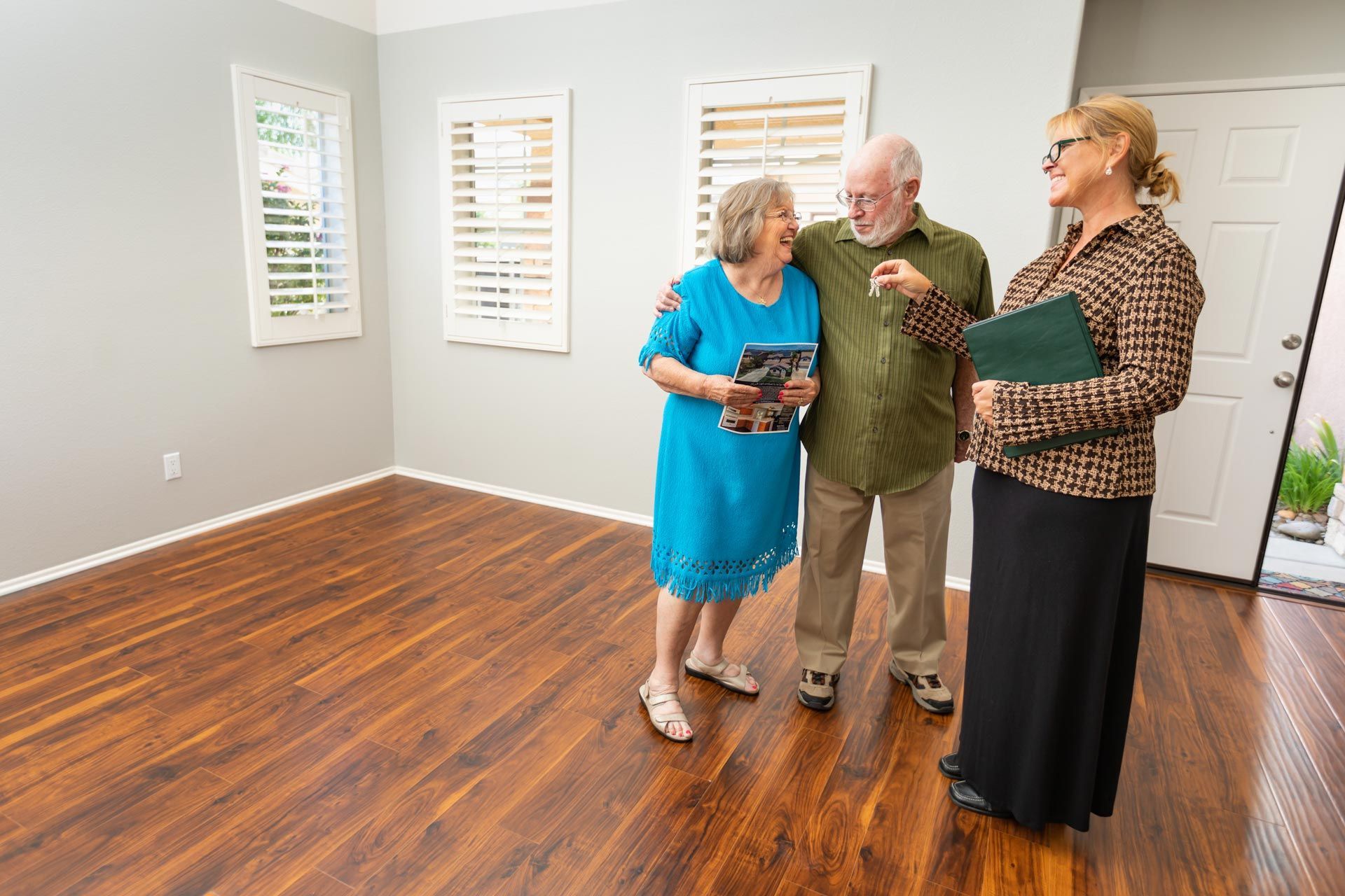 Couple with a real estate agent in an empty room with wood flooring, discussing a property.