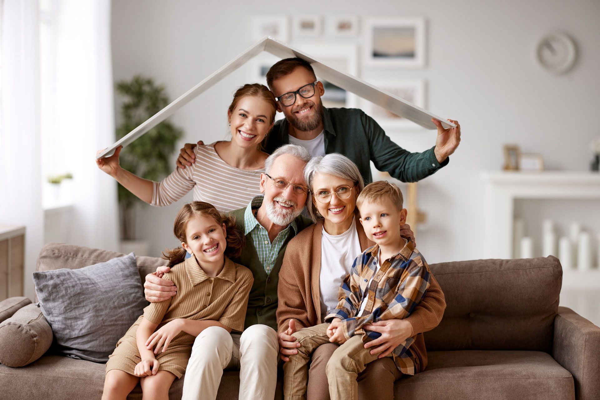 Family of seven smiles for the camera indoors. Adults hold a roof shape over them.