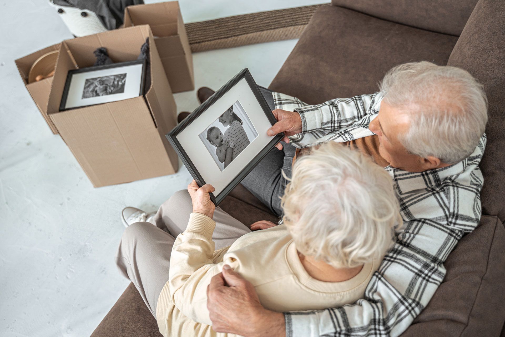 Senior couple looks at framed photo while sitting on a couch near a moving box.