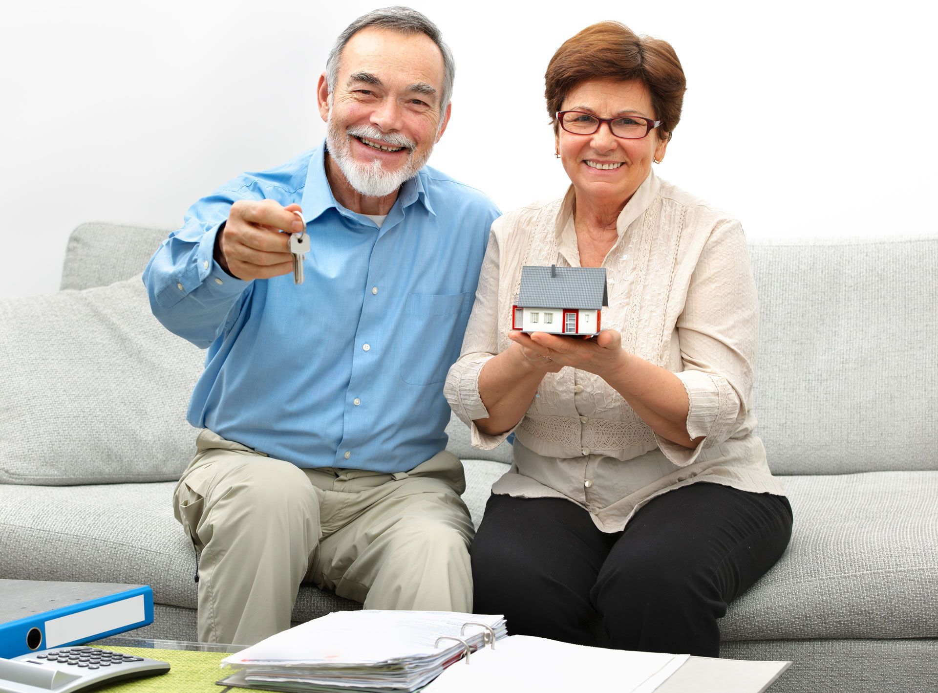 Senior couple holding house keys and a model home, smiling.