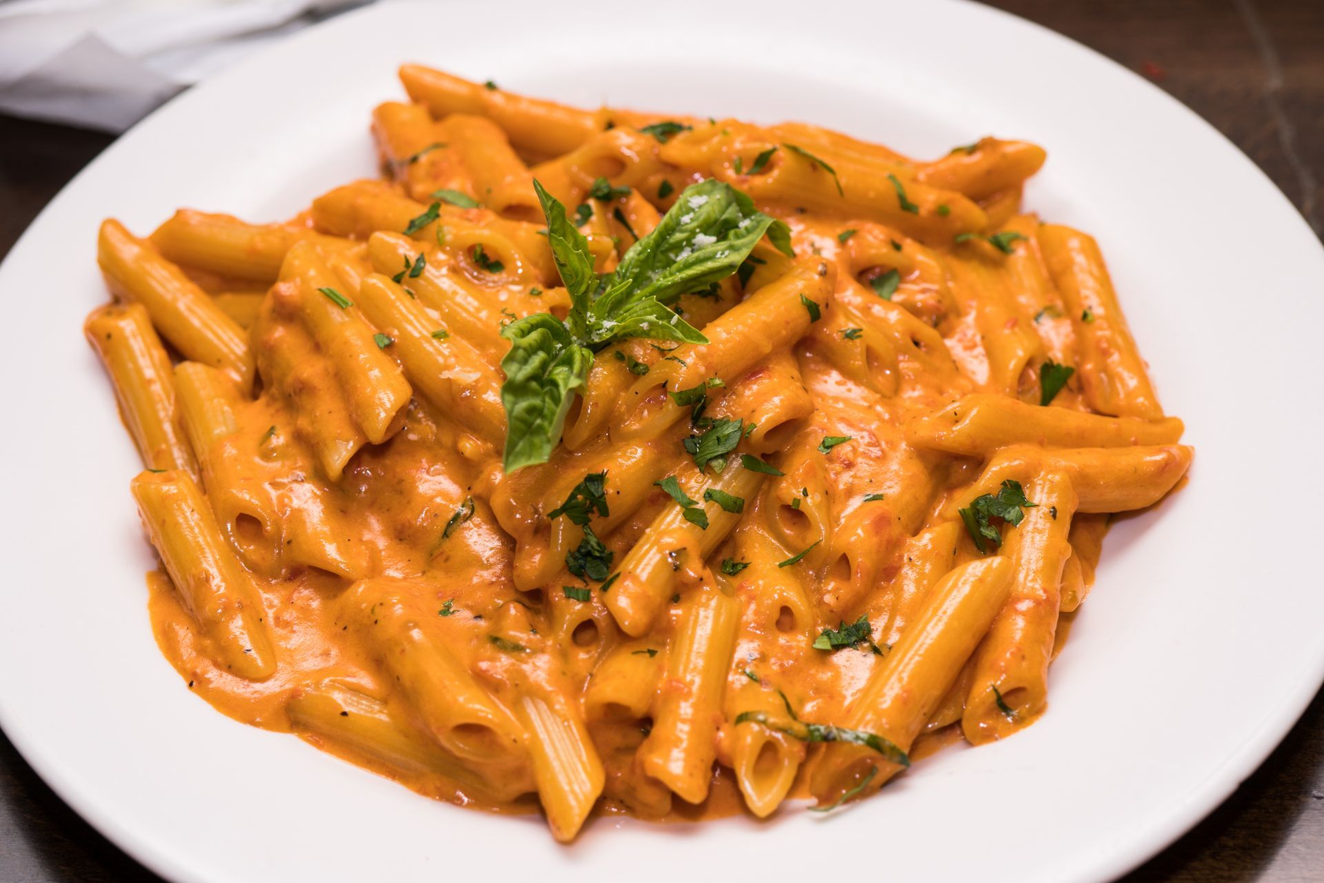 Penne pasta with creamy tomato sauce, garnished with fresh basil, served on a white plate.