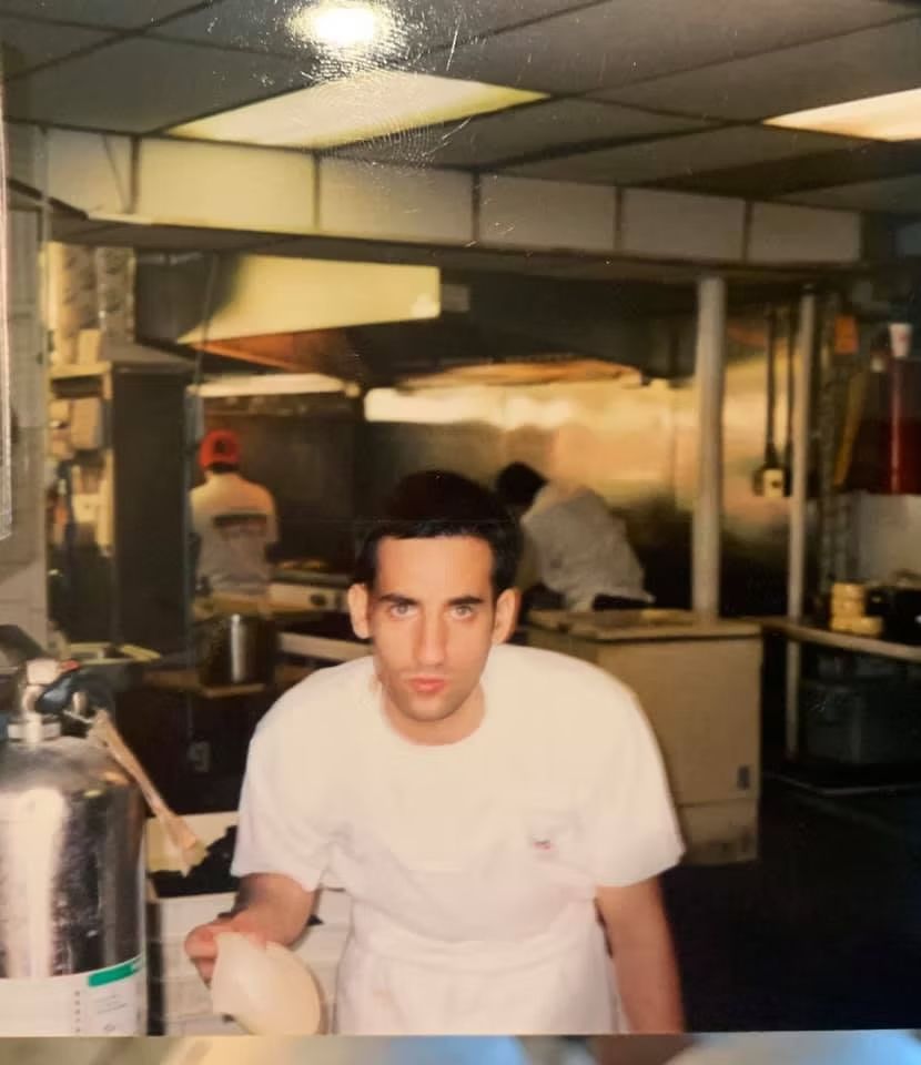 Man in white uniform in a commercial kitchen, looking at the camera.
