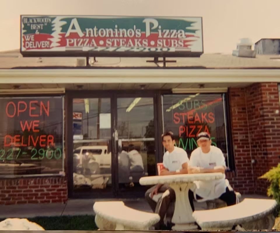 Two men at Antonino's Pizza, outside. Red signage says 