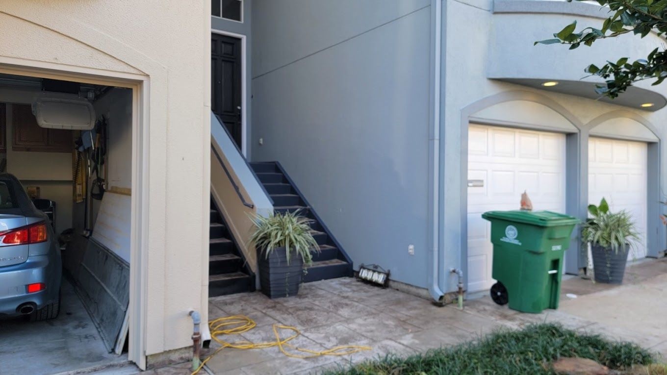 A car is parked in a garage next to a trash can.