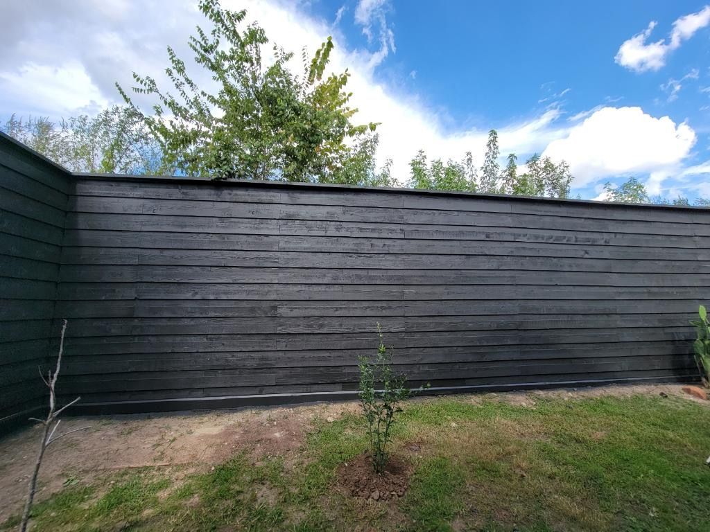 A black wooden fence is surrounded by grass and trees in a backyard.